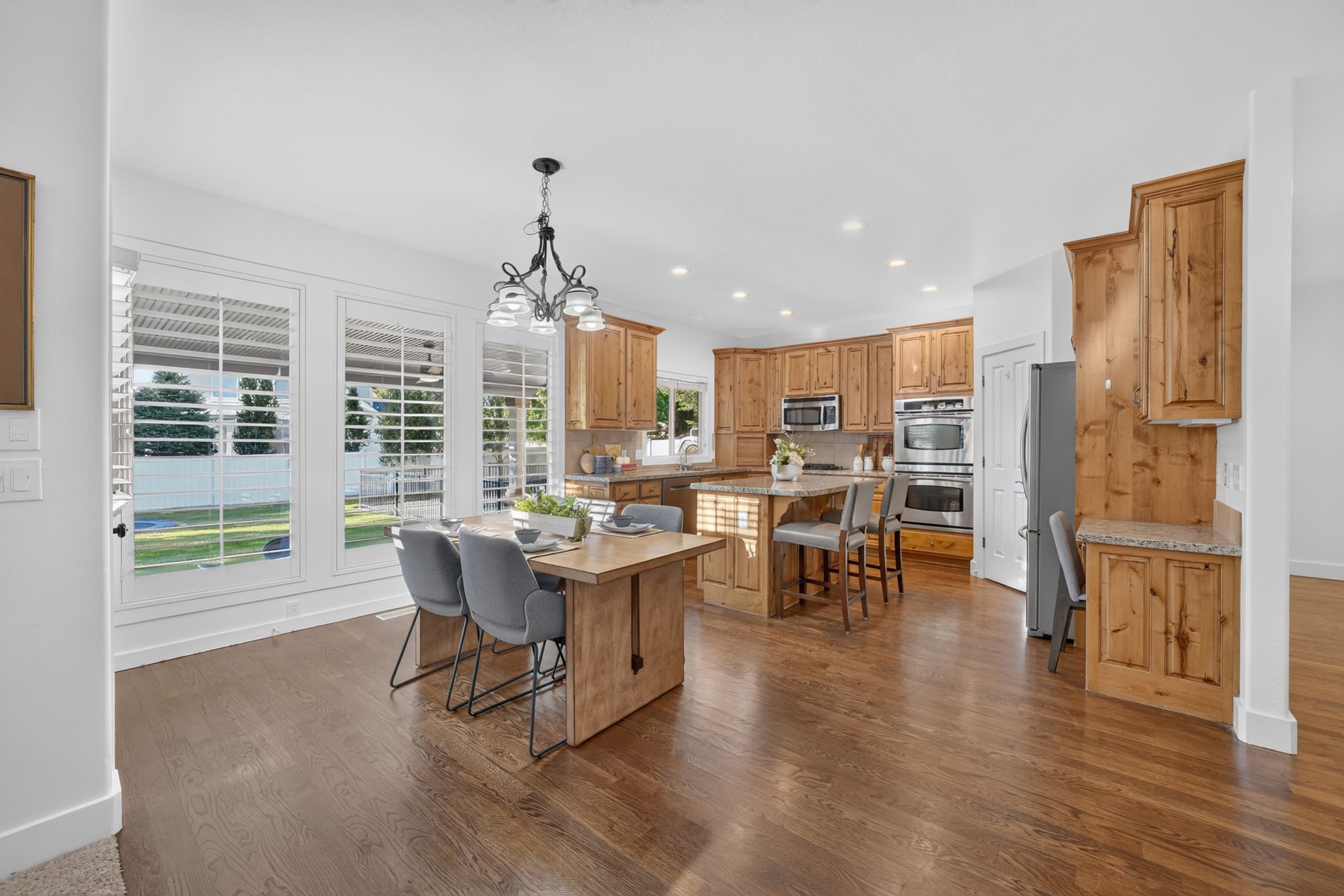 Spacious kitchen and dining area featuring wood-finish flooring, custom wooden cabinetry, stainless steel appliances, and a large kitchen island with counter seating