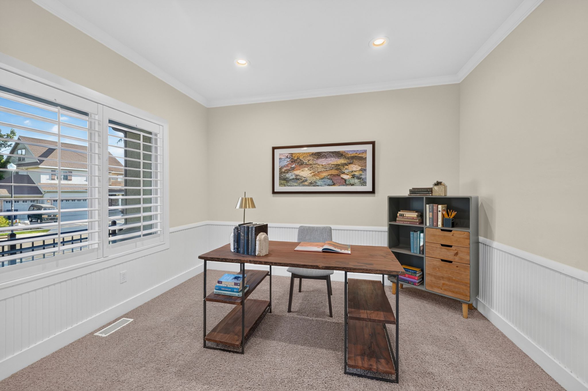 Carpeted room featuring a large window with white plantation shutters, wainscoting, and crown molding