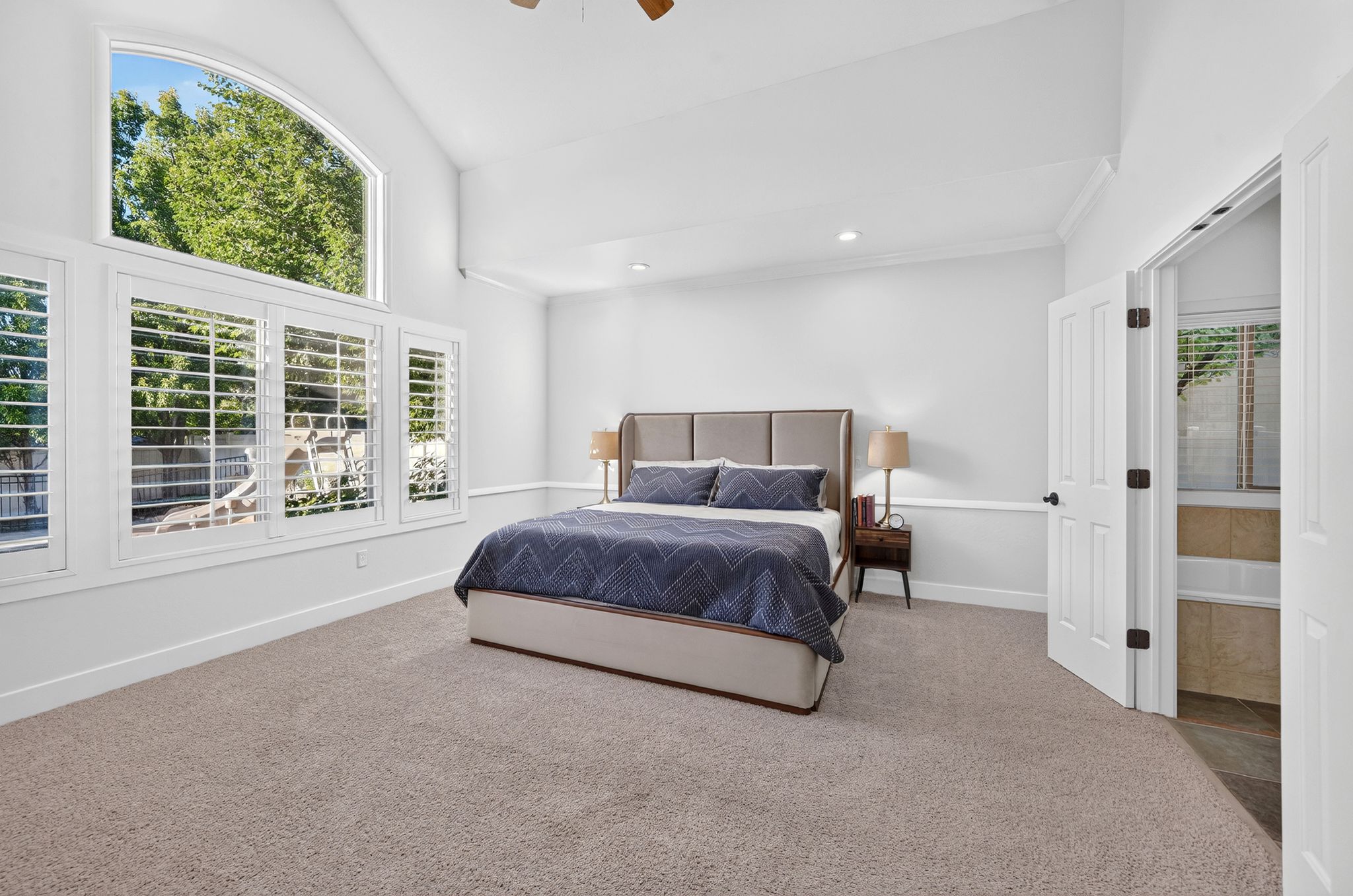Vaulted ceiling bedroom featuring expansive windows with plantation shutters and an arched transom window