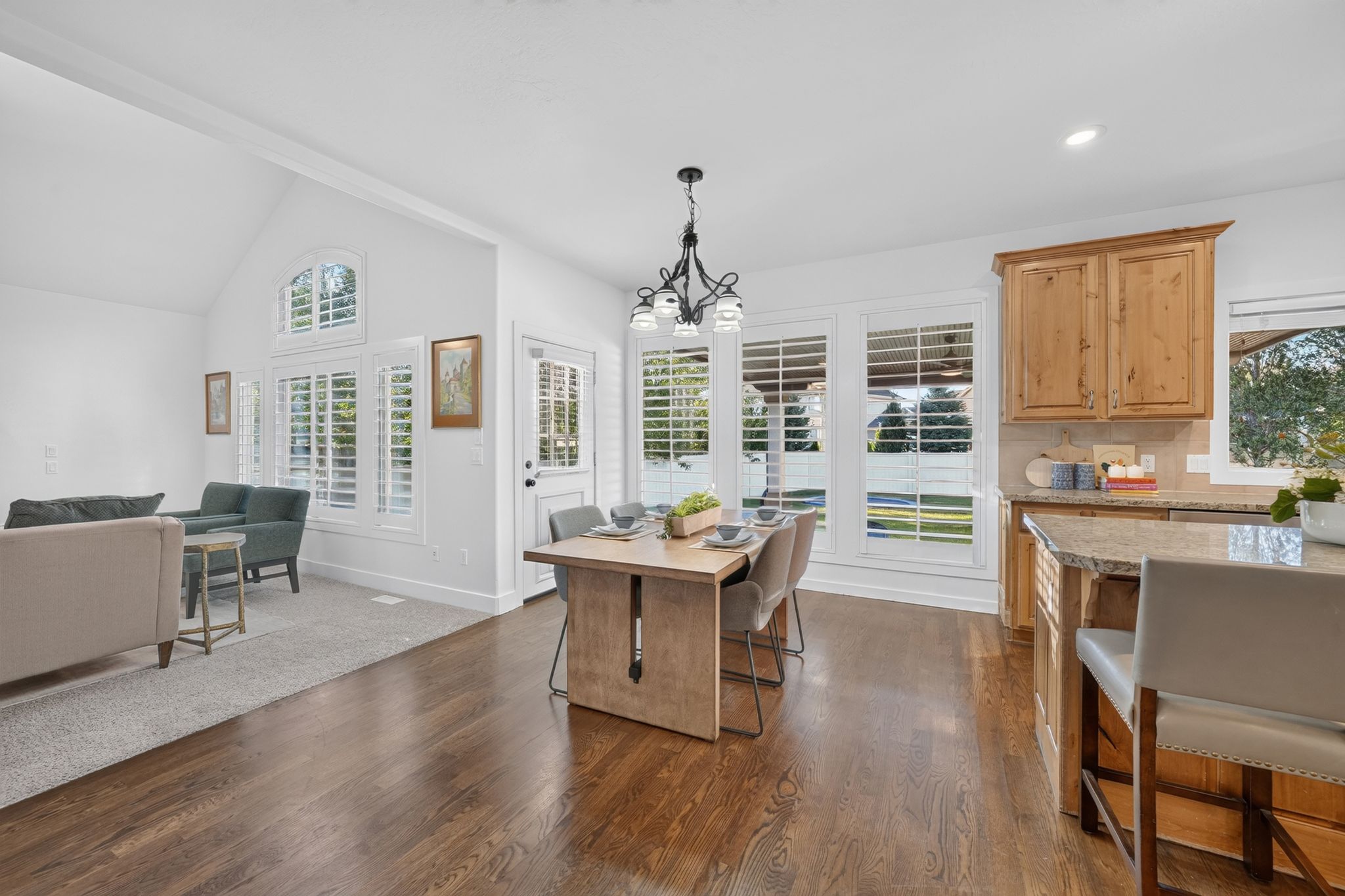 Open-concept living space featuring wood-finish flooring, a kitchen island with seating, natural wood cabinetry, and a dining area with an overhead chandelier