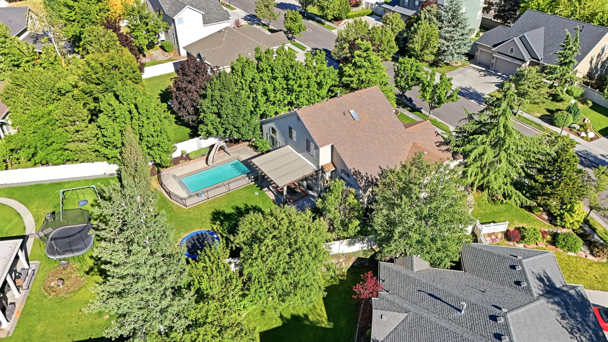 Expansive backyard featuring a fenced swimming pool with deck surround, an adjacent covered patio, and mature trees