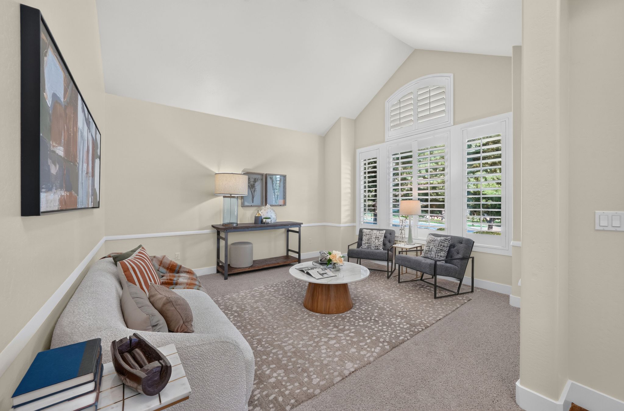 Vaulted ceiling living area featuring a large window array with plantation shutters, a decorative arched window, and neutral wall tones