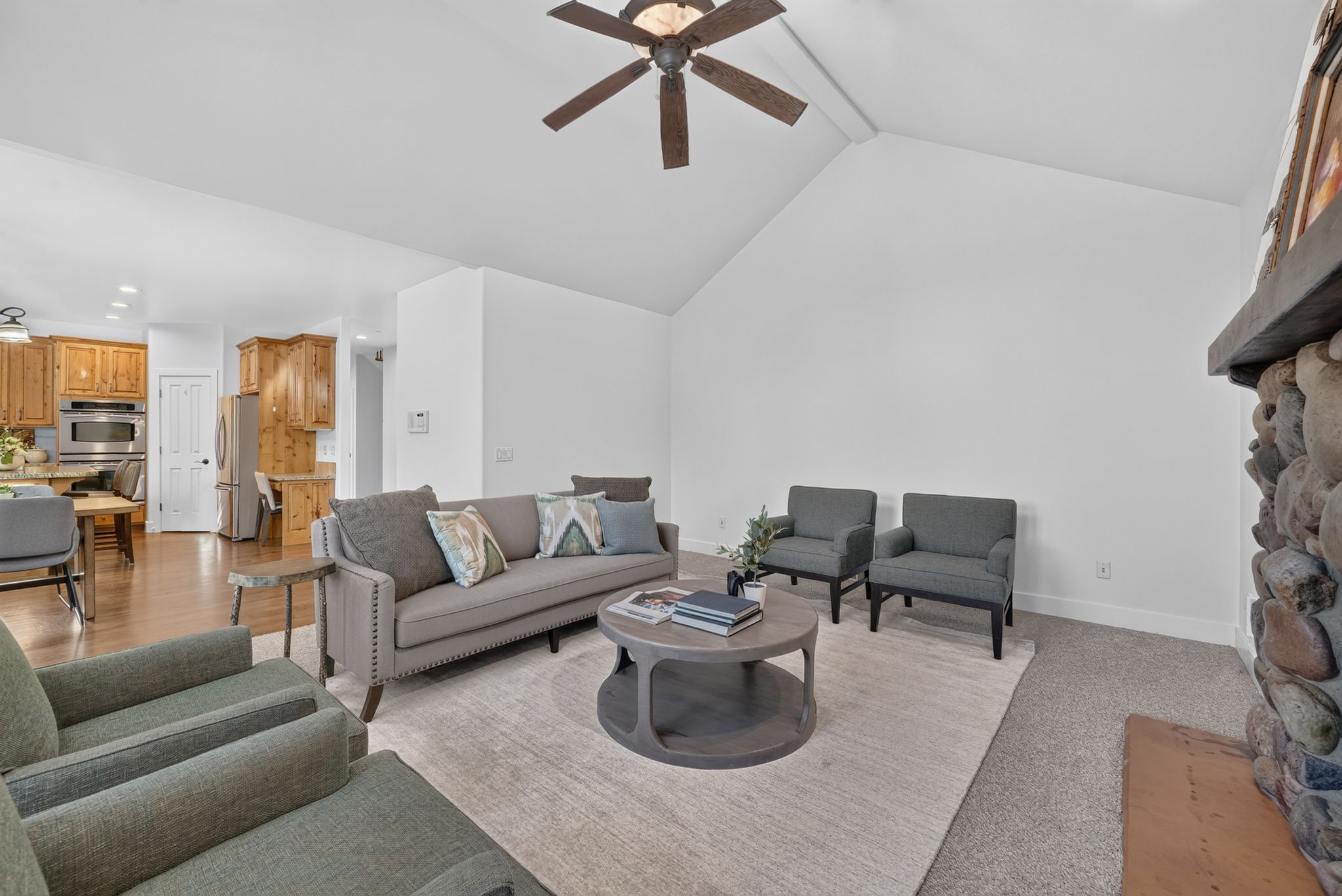 Living area featuring a vaulted ceiling with a ceiling fan, a stone fireplace with a wood mantle, and carpet flooring