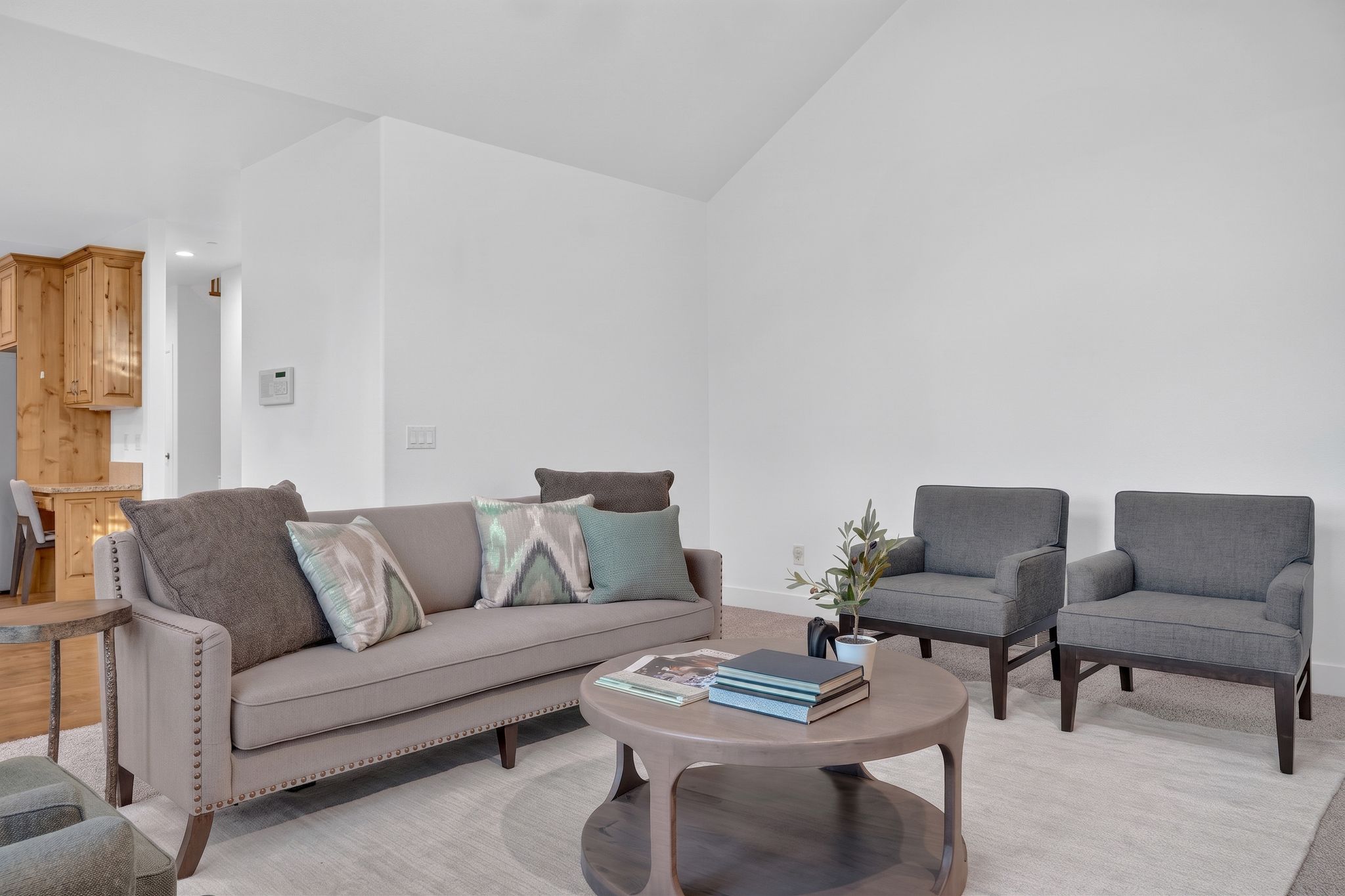 Living space featuring vaulted ceilings, light-toned carpeting, and a partial view of a kitchen with wood cabinetry