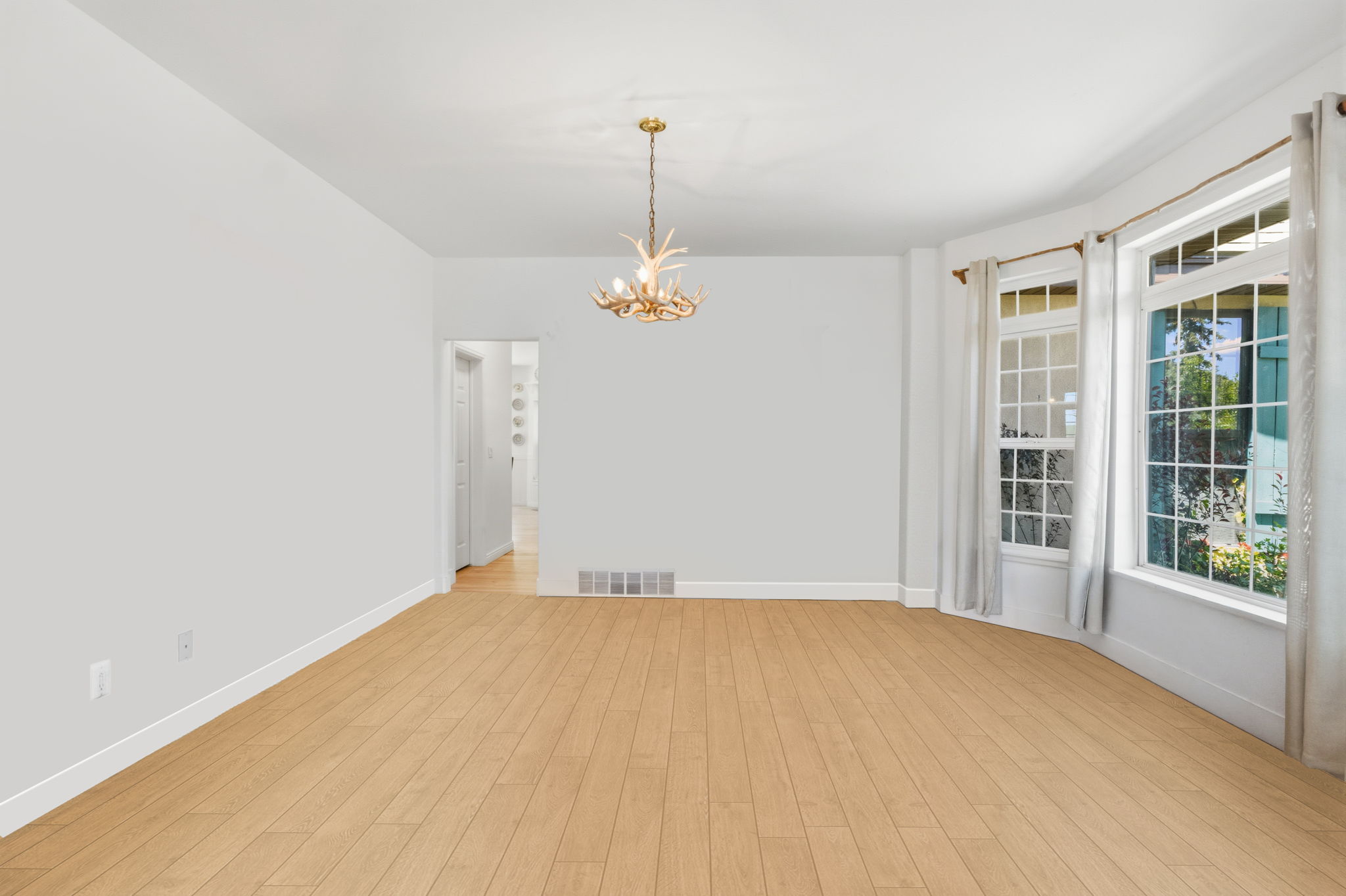 Bright interior space featuring light wood-finish flooring, a unique antler-style chandelier, and multiple large windows