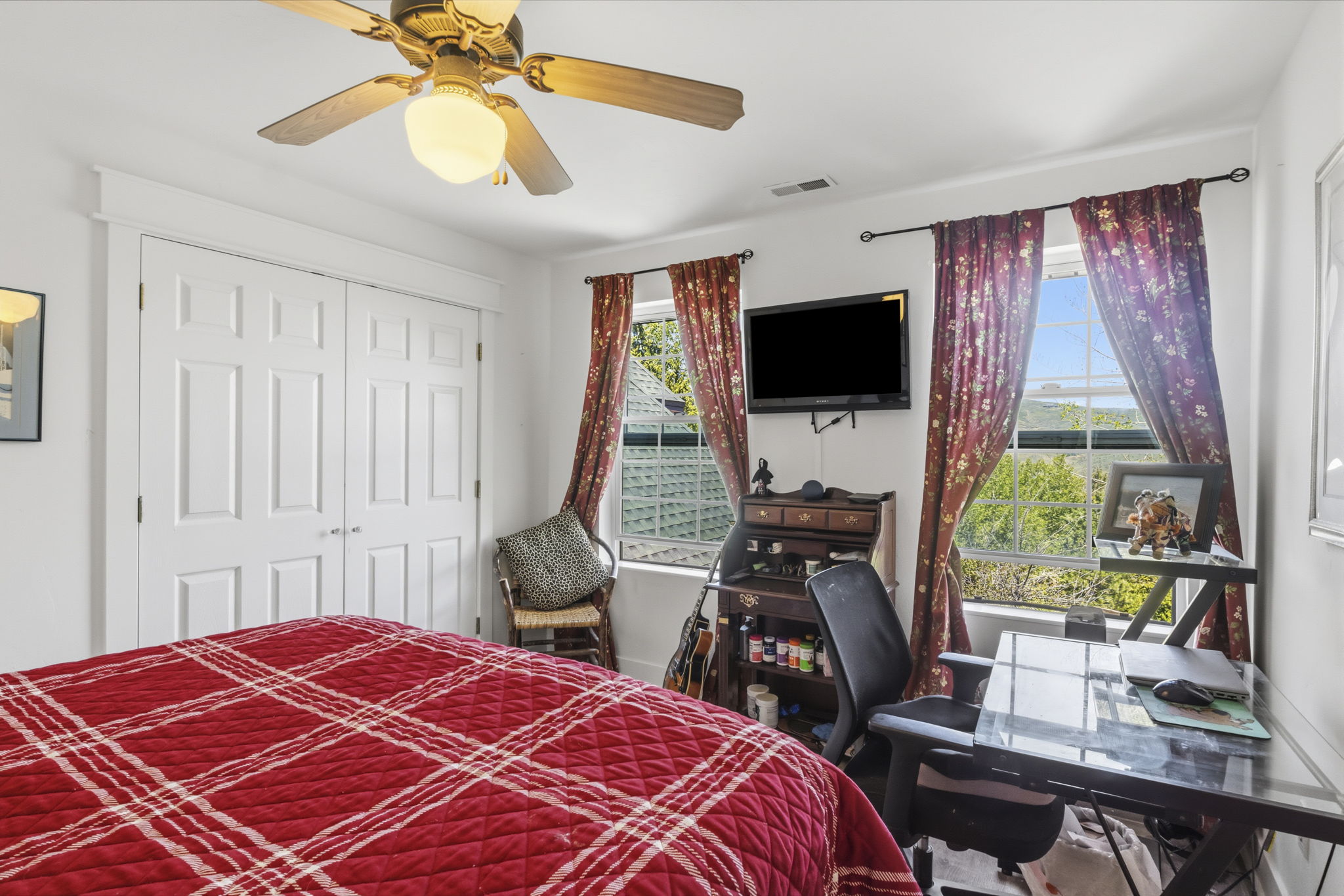 Bedroom featuring twin paneled closet doors, a ceiling fan with integrated lighting, and two windows providing exterior visibility