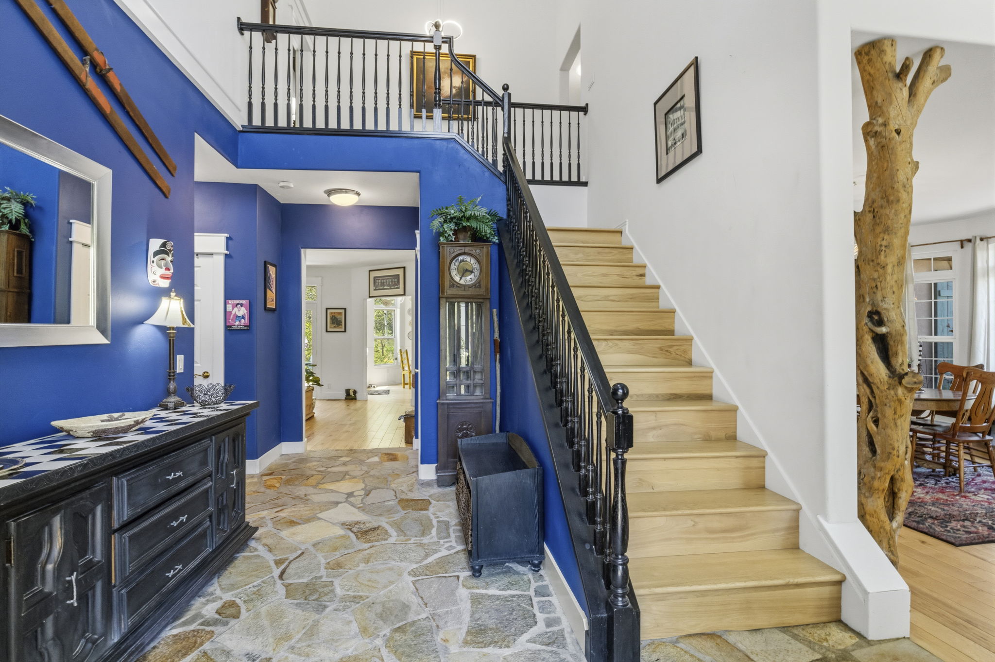 Two-story entryway featuring a natural stone flagstone floor, a grand staircase with wood treads and black balusters, and a natural wood column