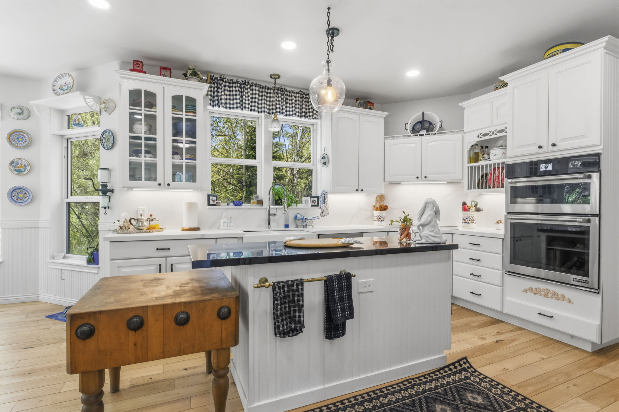 Kitchen featuring white cabinetry, a central island with a dark countertop, stainless steel double wall ovens, wood-finish flooring, and multiple windows