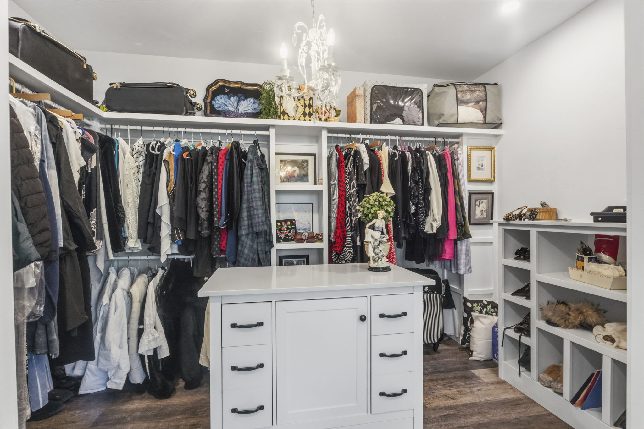 Spacious custom closet featuring a central island with storage, extensive hanging racks, built-in shelving, wood-finish flooring, and a decorative chandelier
