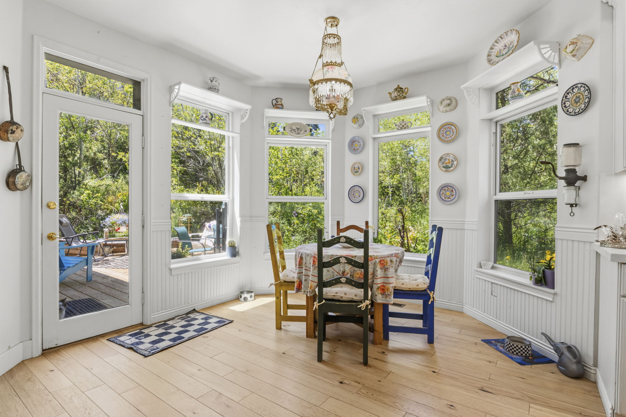 Dining space featuring light wood-finish flooring, multiple large windows, a glass-paneled door opening to a deck, and beadboard wainscoting