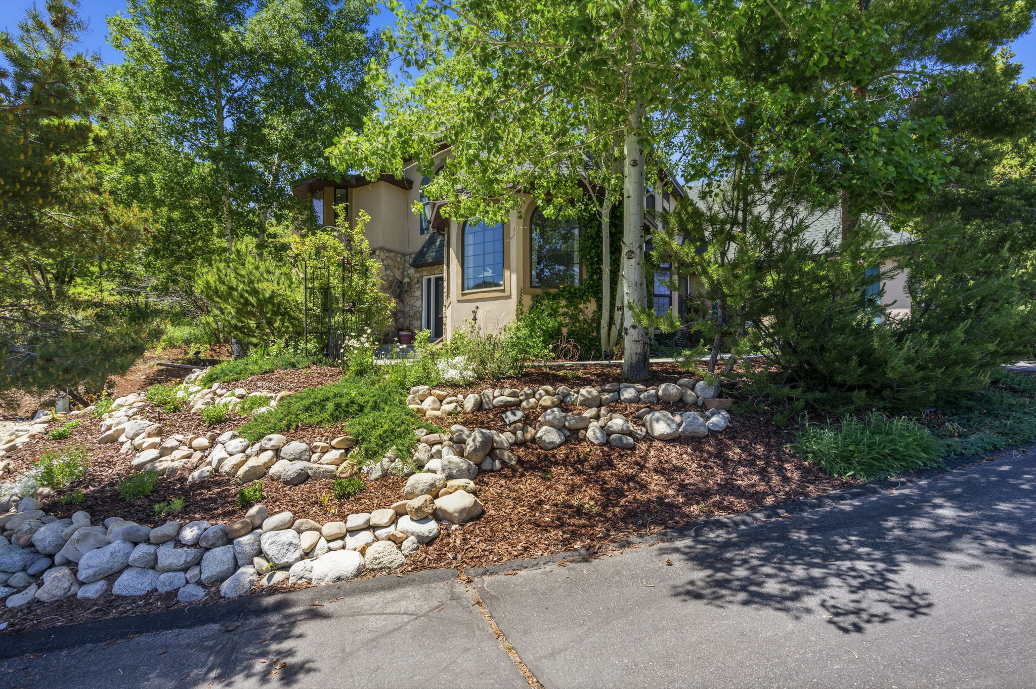 Property exterior featuring a stucco and stone facade, arched windows, and mature trees