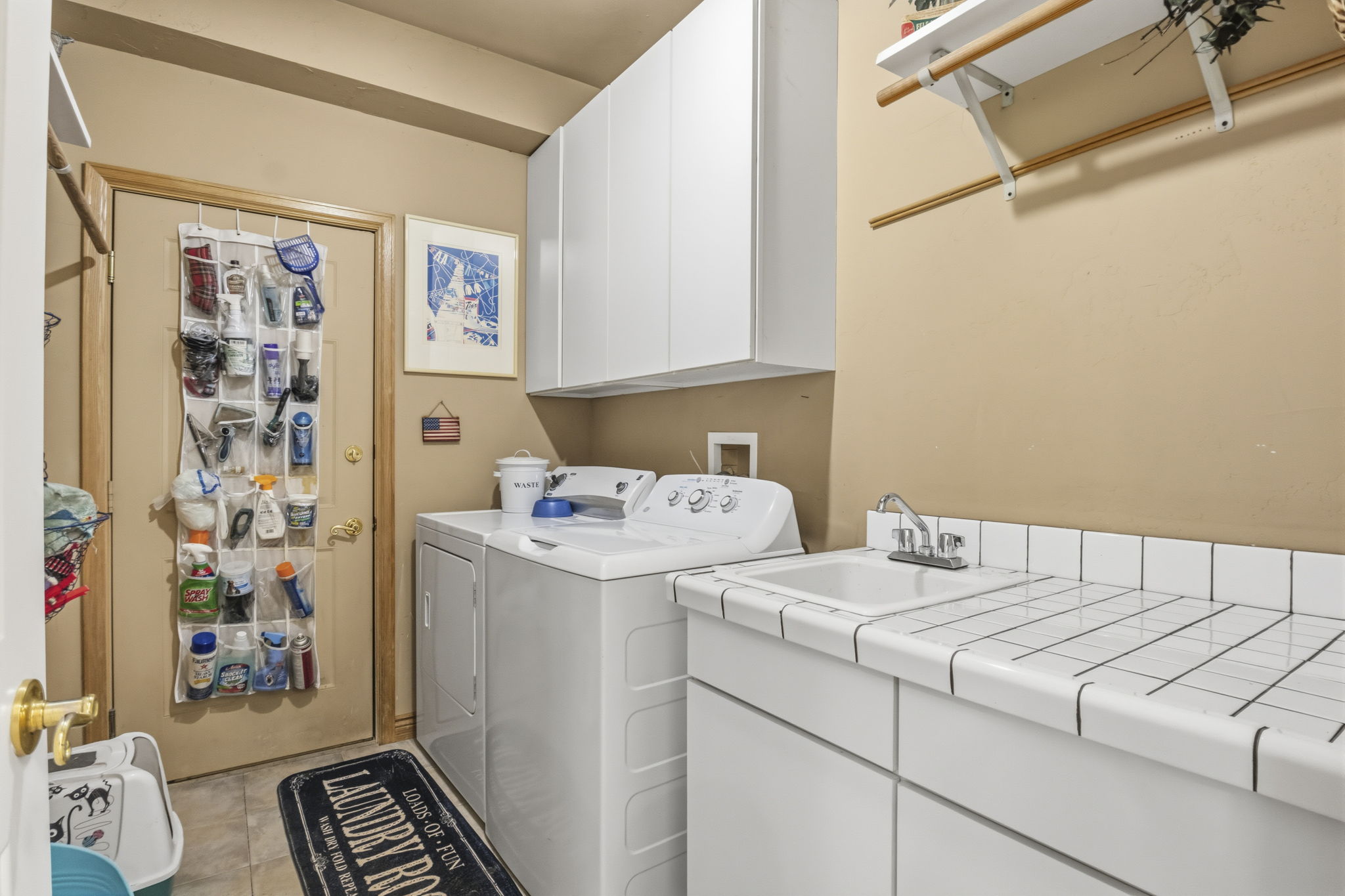 Dedicated laundry area featuring a utility sink, white tiled countertop, white upper and lower cabinetry, and wood-finish flooring