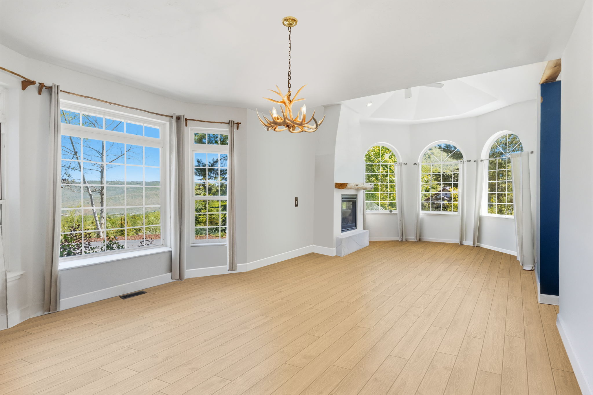 Bright living area featuring wood-finish flooring, a built-in fireplace with a stone surround, and multiple picture windows