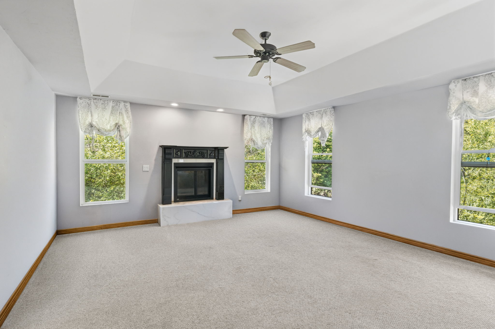 Spacious interior room featuring a decorative fireplace with a dark mantel and hearth, tray ceiling, recessed lighting, and a ceiling fan