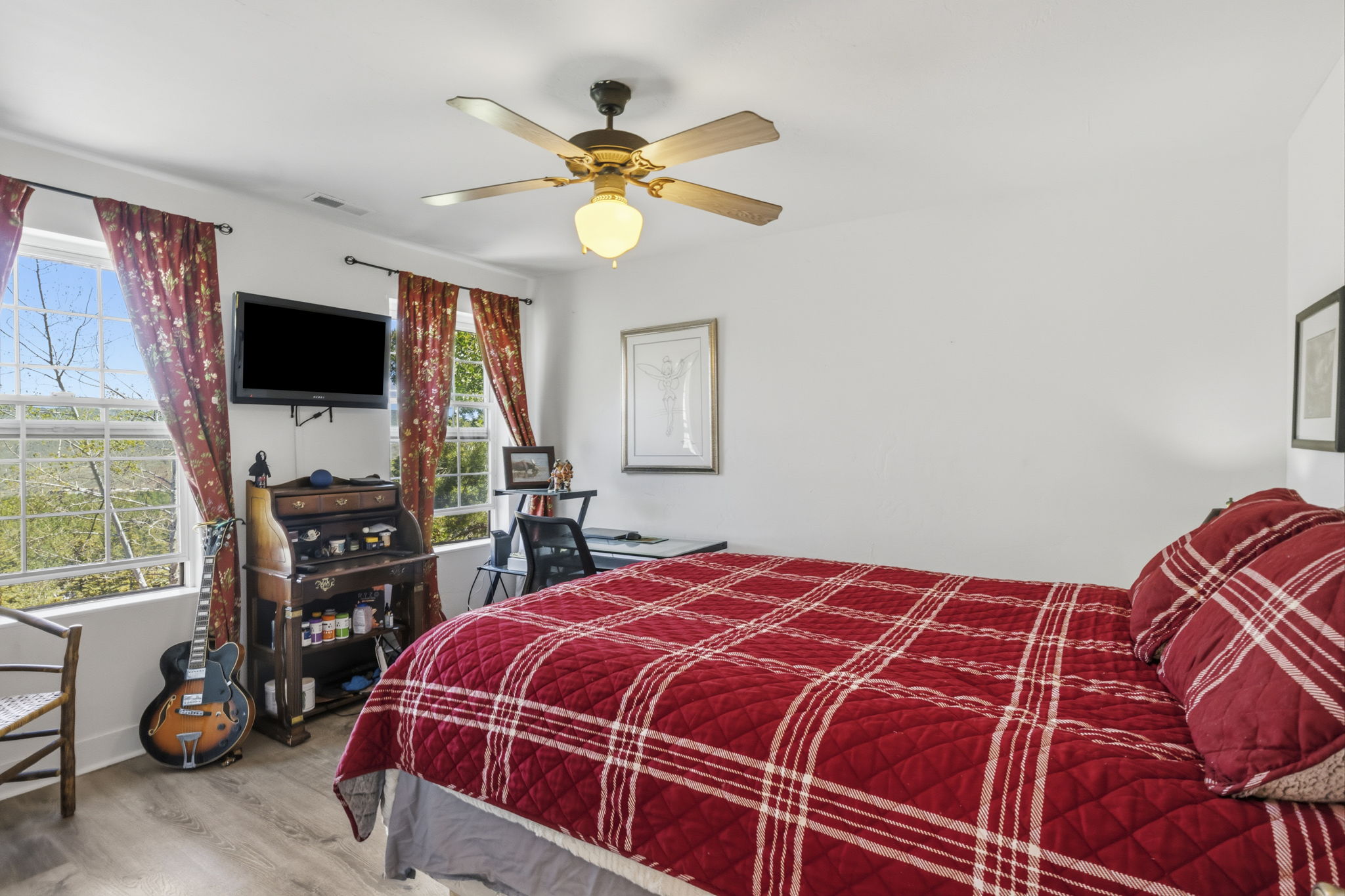 Bright room featuring multiple windows with tree-lined scenery, light wood-finish flooring, a ceiling fan with integrated lighting, and white walls
