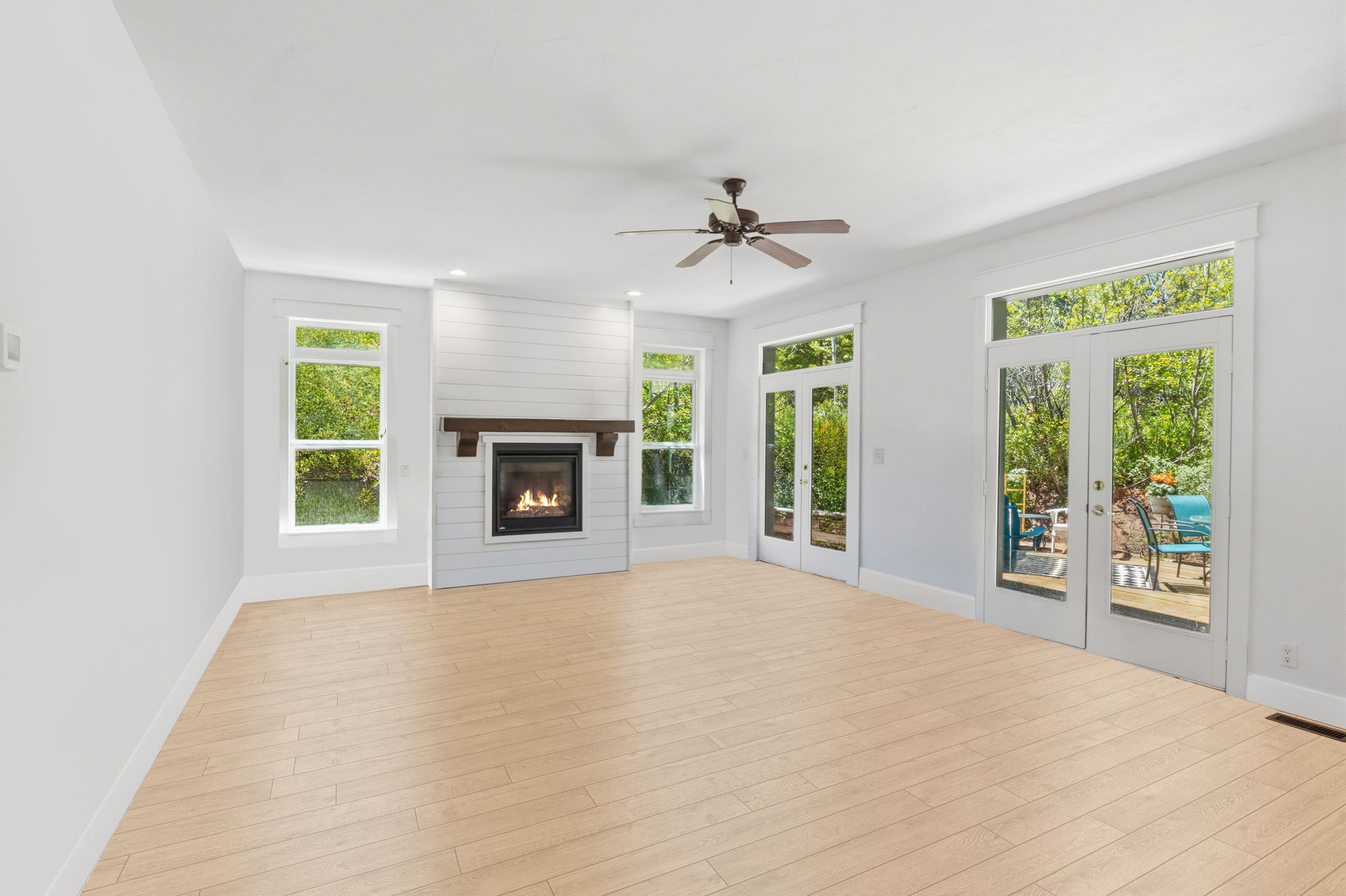 Bright living space featuring wood-finish flooring, a contemporary fireplace with shiplap surround and wood mantel, multiple large windows, and two sets of glass-paned French doors