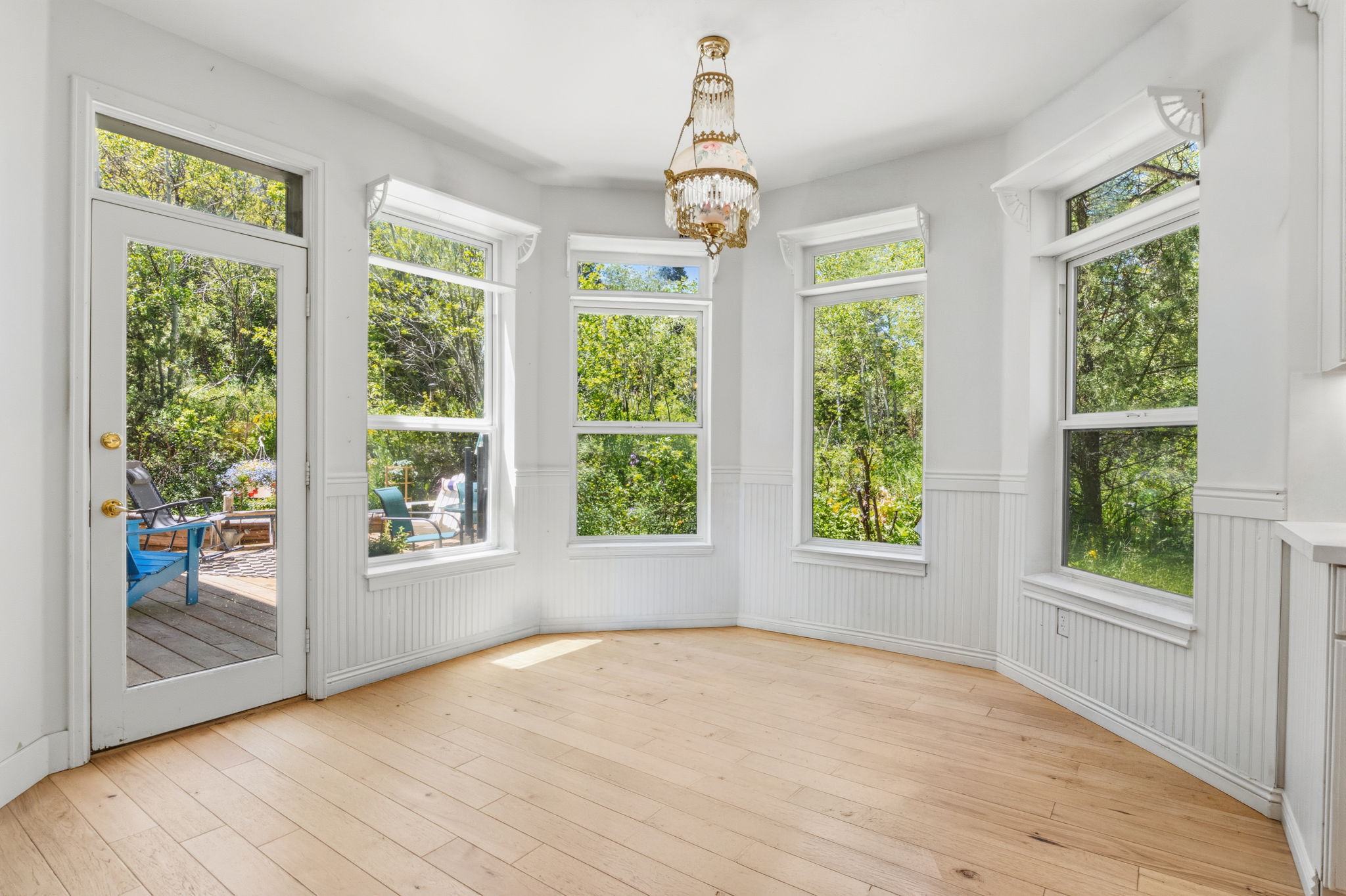 Bay window area featuring light wood-finish flooring, white beadboard wainscoting, and a decorative chandelier