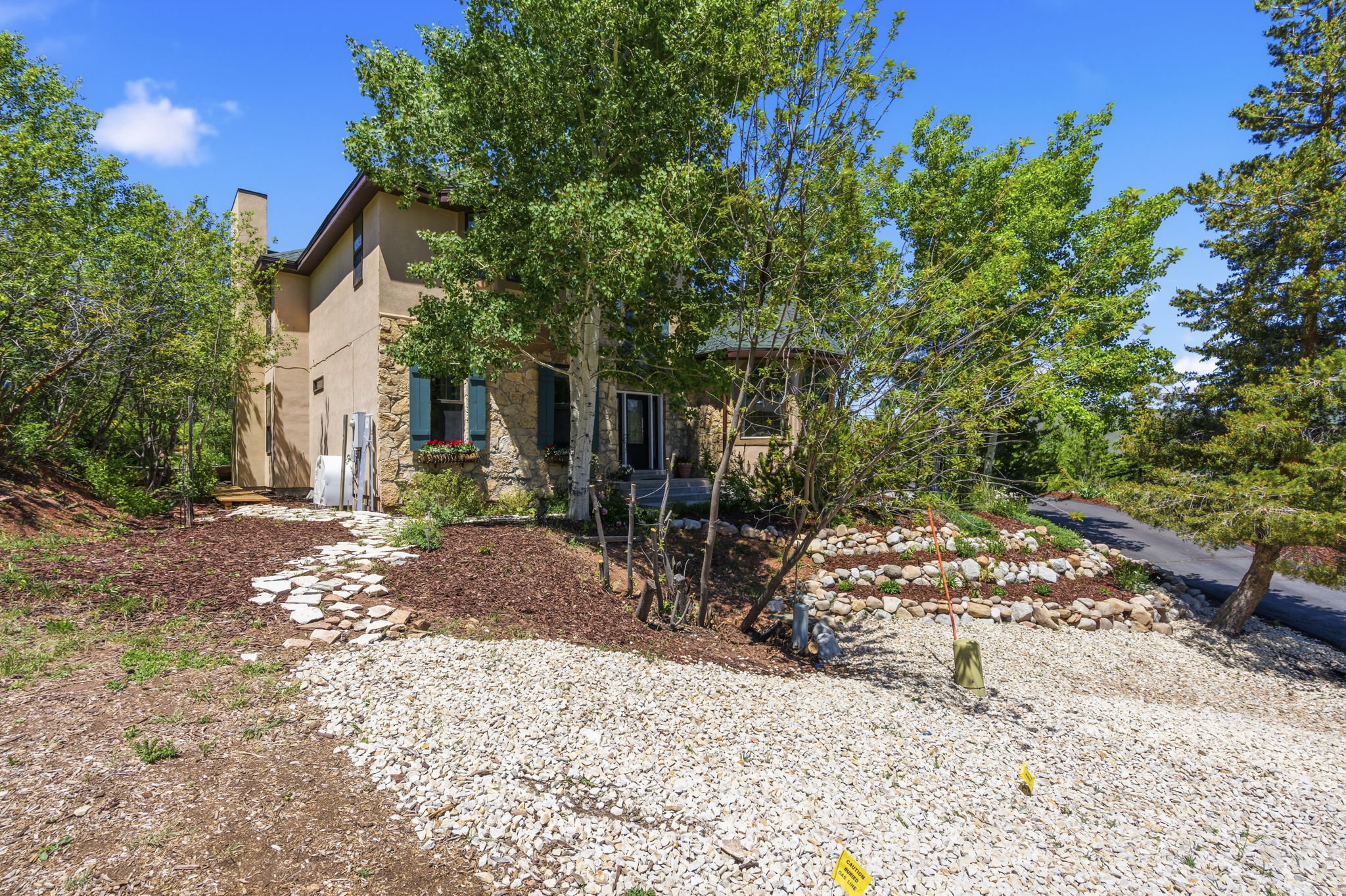 Stone and stucco exterior featuring a partial stone facade, green window shutters, a stone pathway, and mature trees