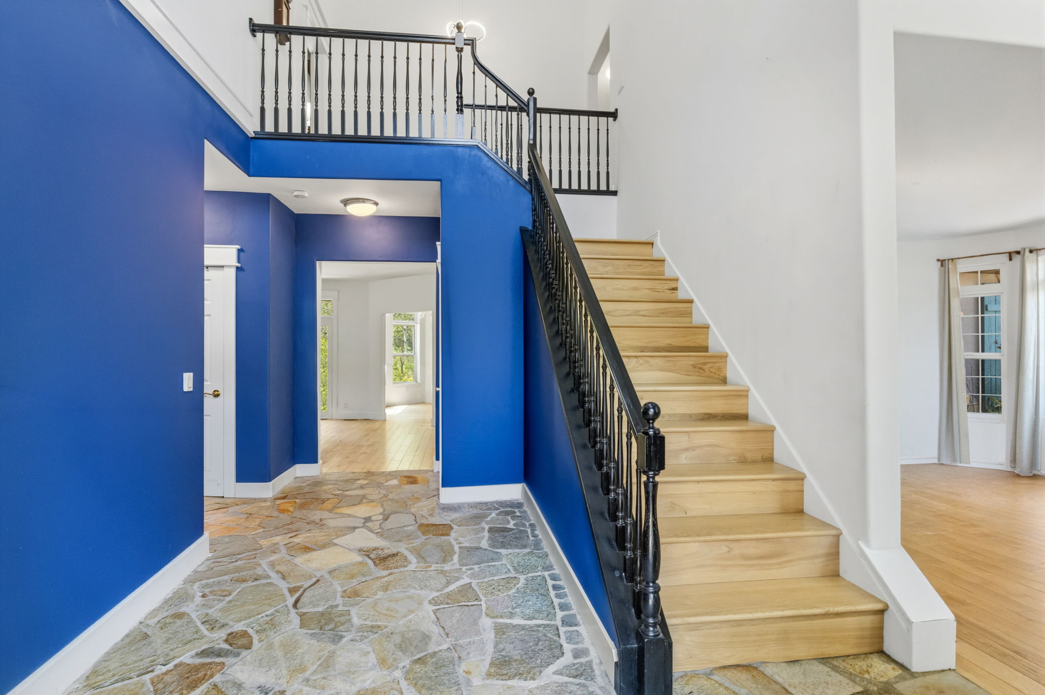 Foyer featuring natural stone tile flooring, a staircase with wood treads and black balusters, and a second-story landing with matching railing