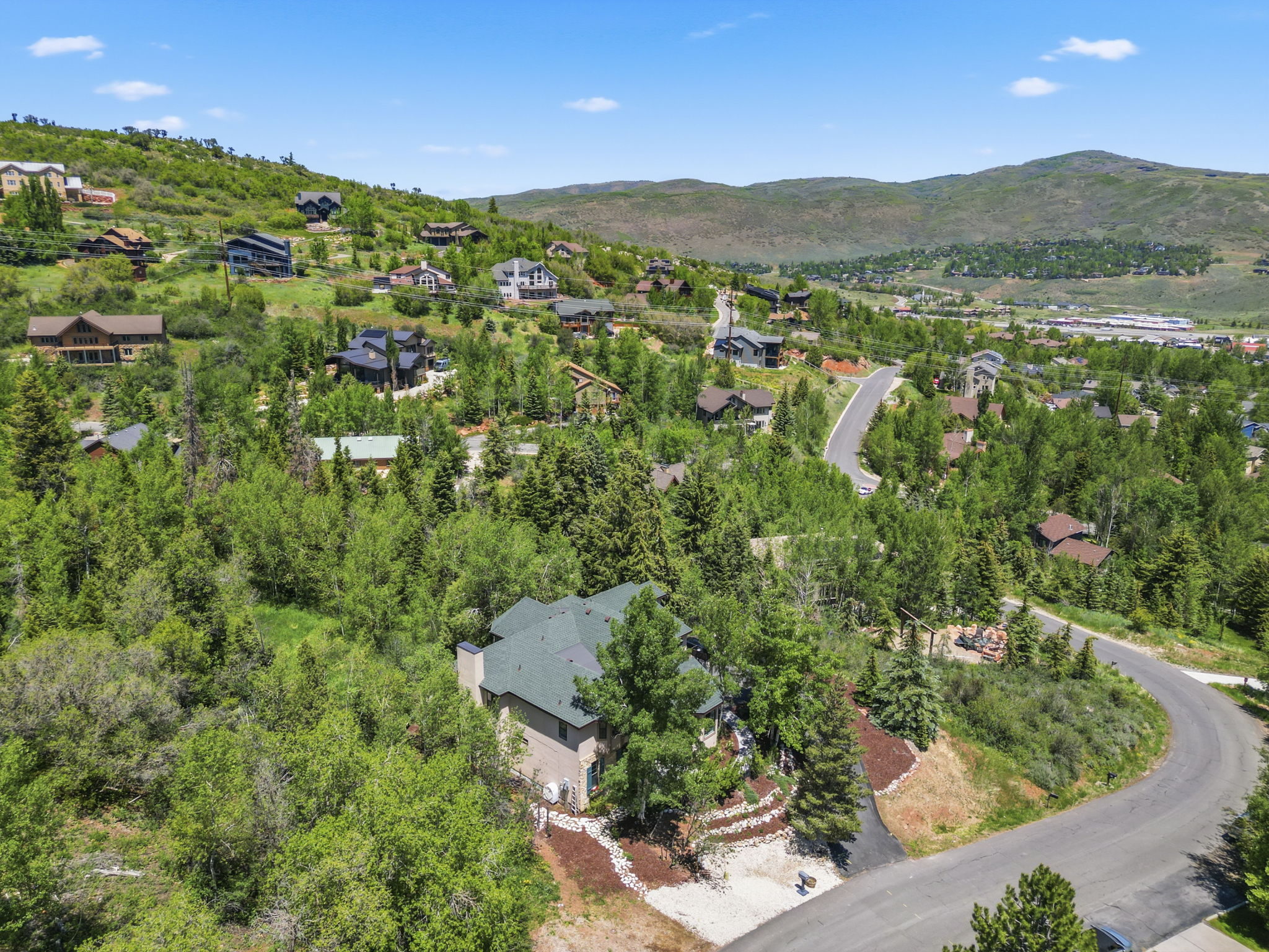 Hillside property featuring a multi-level exterior, dark shingle roof, mature landscaping, and a paved driveway
