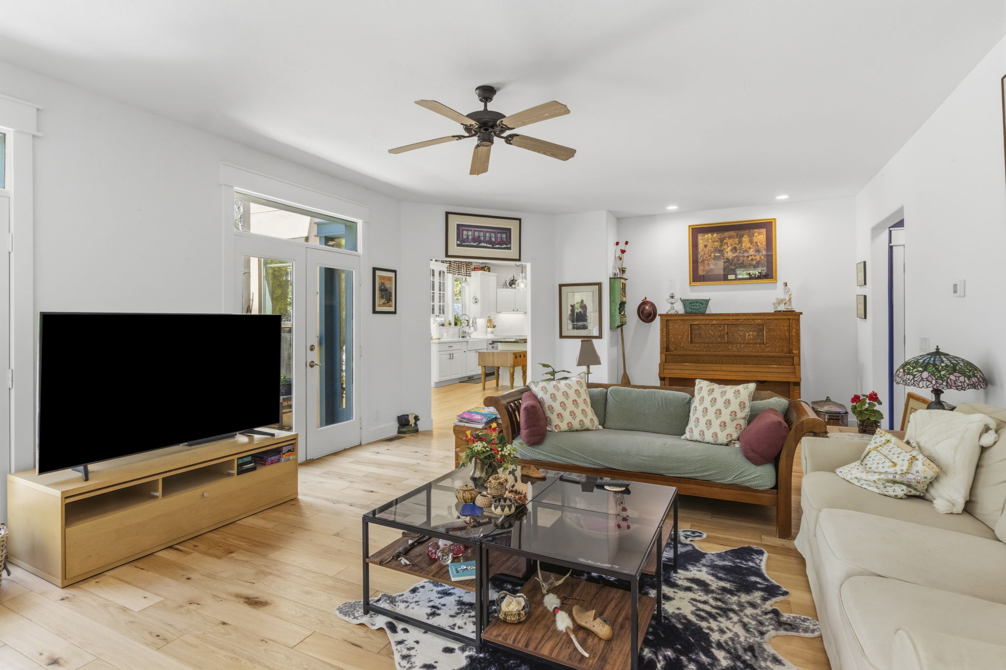 Open-concept living area featuring light wood-finish flooring, white walls, and a ceiling fan