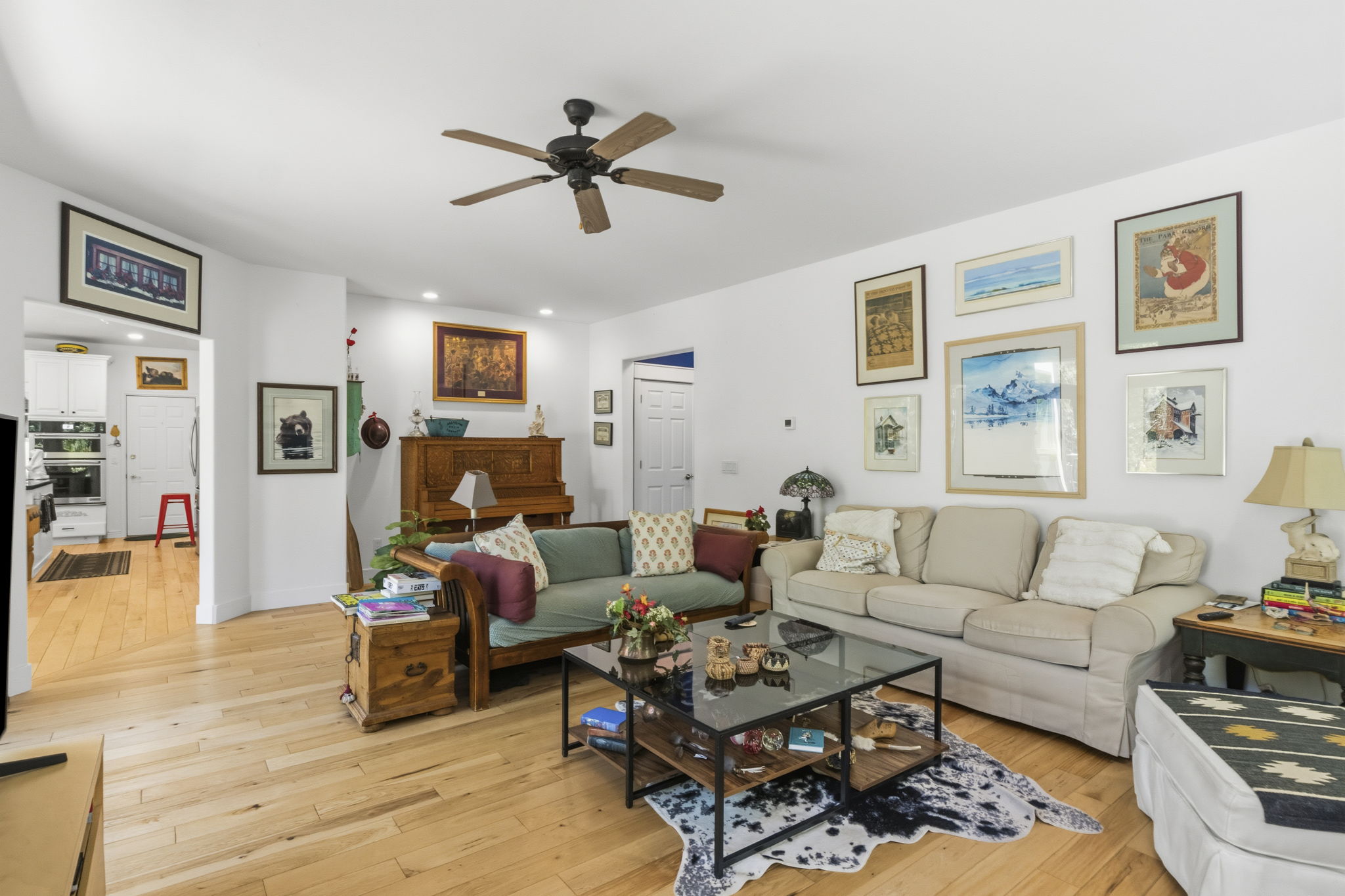 Bright open-concept living area featuring light wood-finish flooring, a ceiling fan, recessed lighting, and white walls