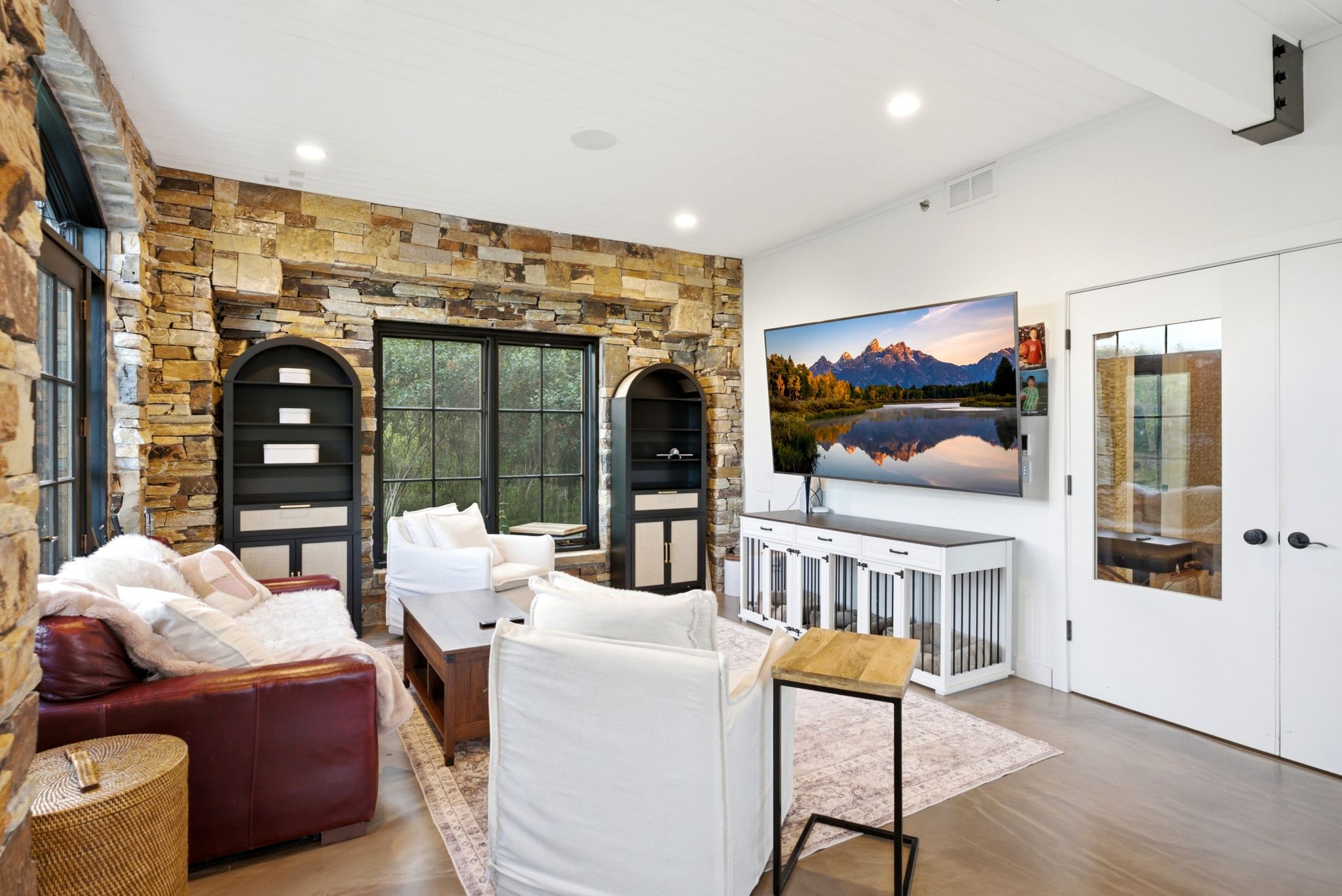 Living area featuring a natural stone accent wall with built-in arched shelving, large black-framed windows, and light-tone flooring