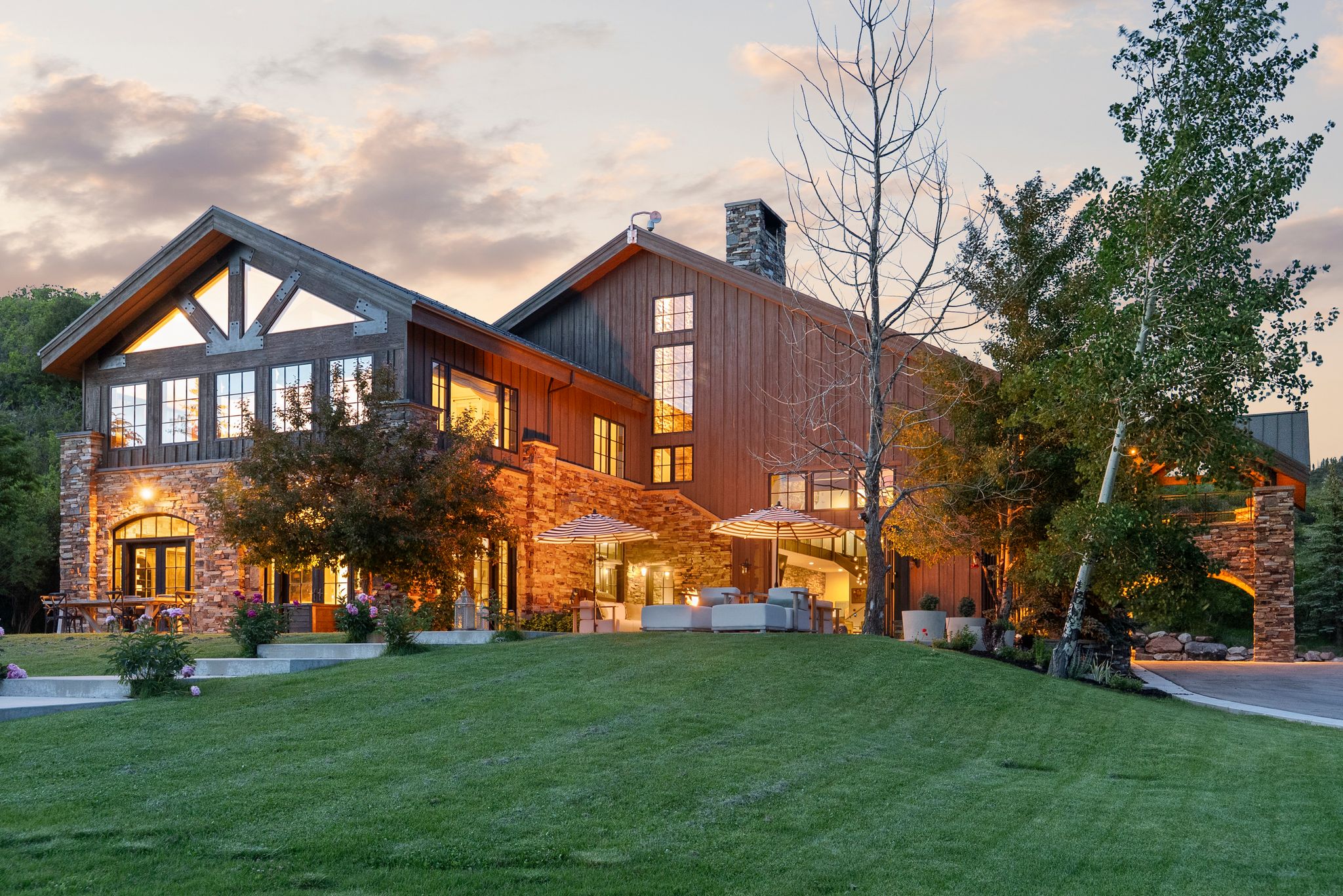 Expansive property featuring a stone and wood-sided exterior, a manicured lawn, and multiple outdoor patio areas