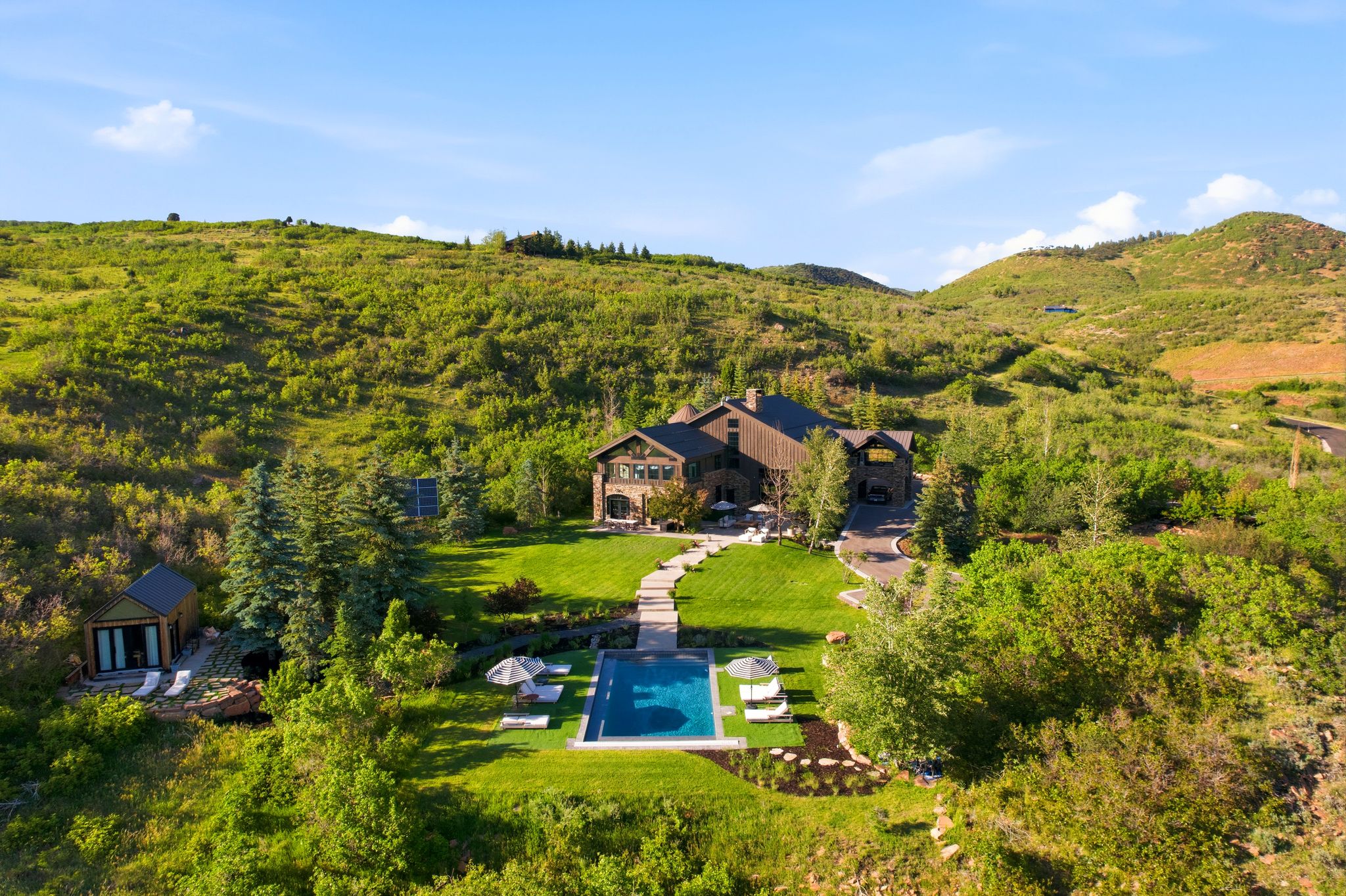 Stone and wood-clad residence with a rectangular swimming pool, expansive lawn, and mature landscaping