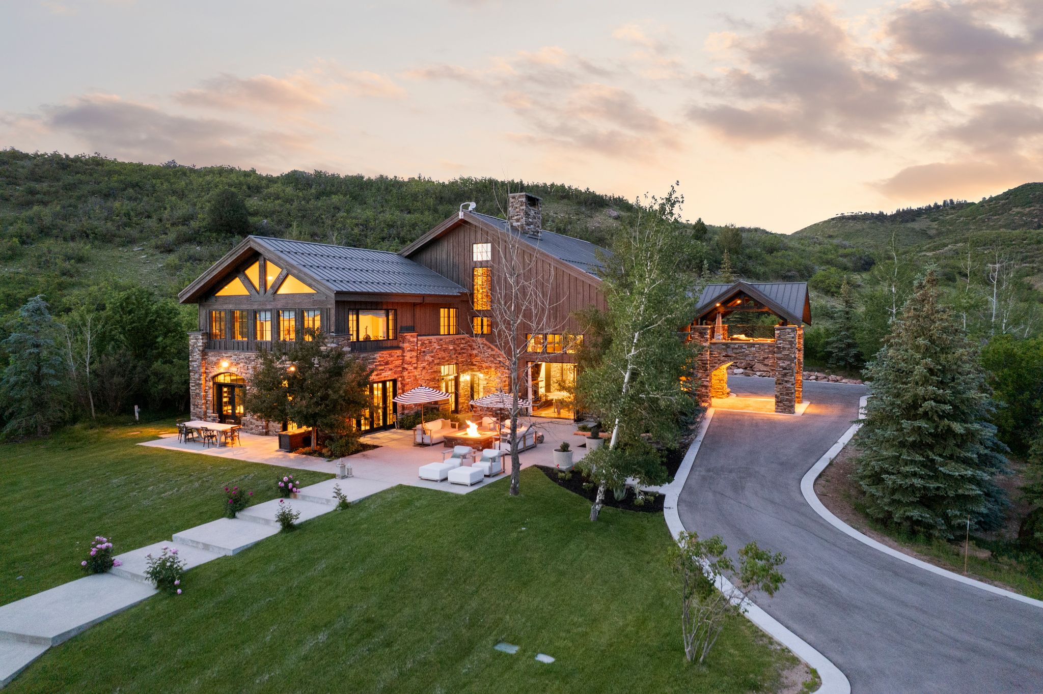 Stone and wood-sided architectural residence featuring a metal roof, an expansive patio, a private driveway, and a covered entry archway