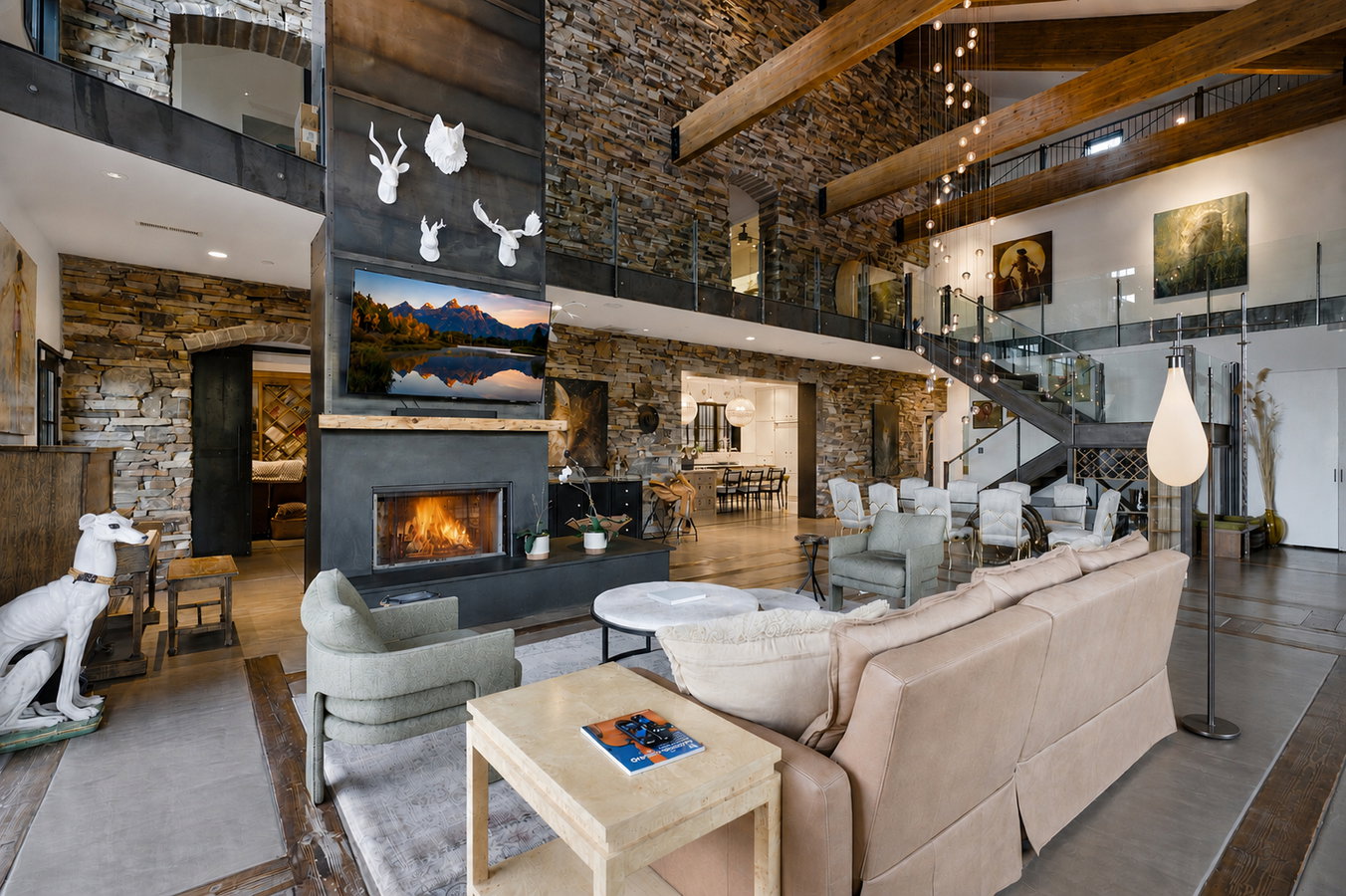 Grand living area featuring a stone accent wall, soaring ceilings with exposed wood beams, and a central fireplace with an integrated media display