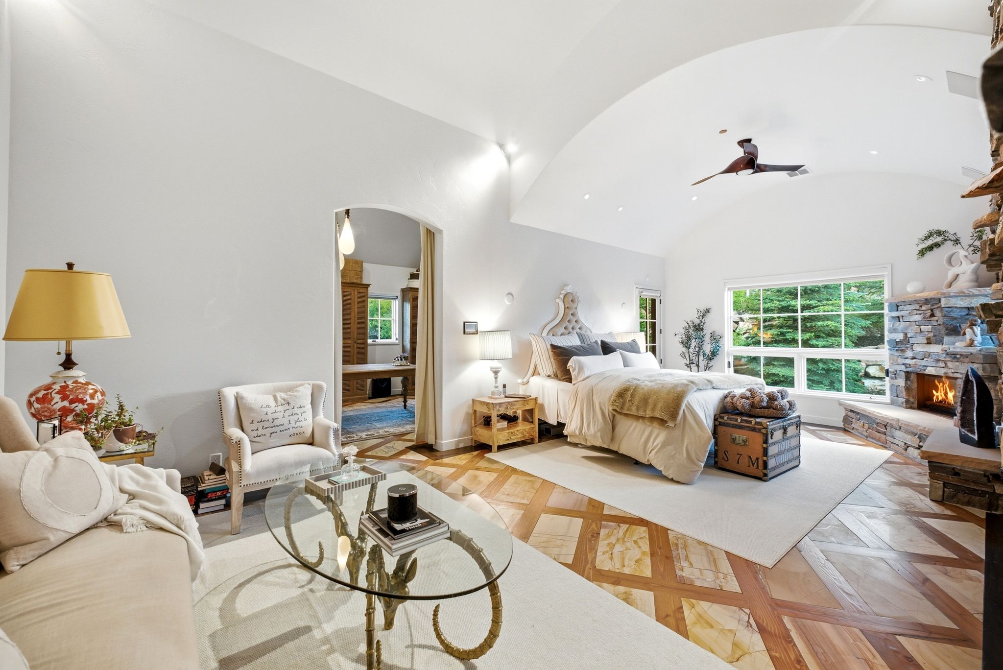 Vaulted ceiling bedroom featuring a stone-clad fireplace and large picture window