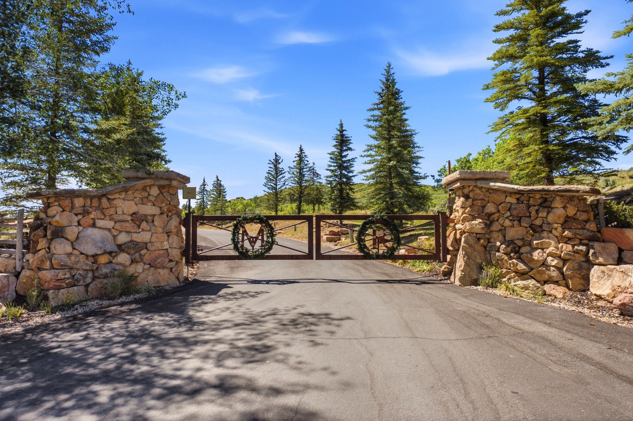 Paved driveway leading to a gated entrance with stone pillar supports