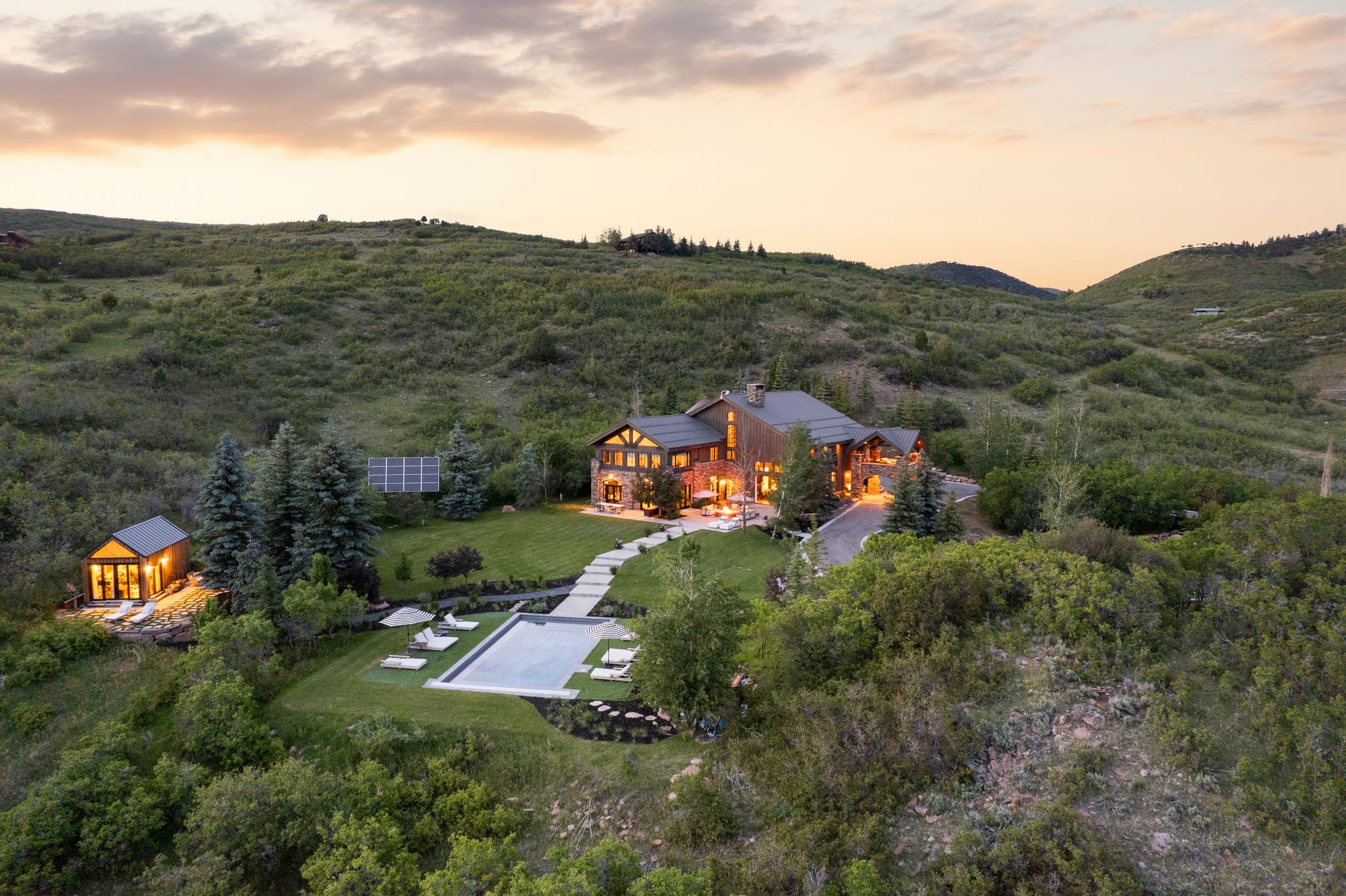 Crafted stone and timber residence with a large outdoor pool, accompanying pool house, and a manicured lawn