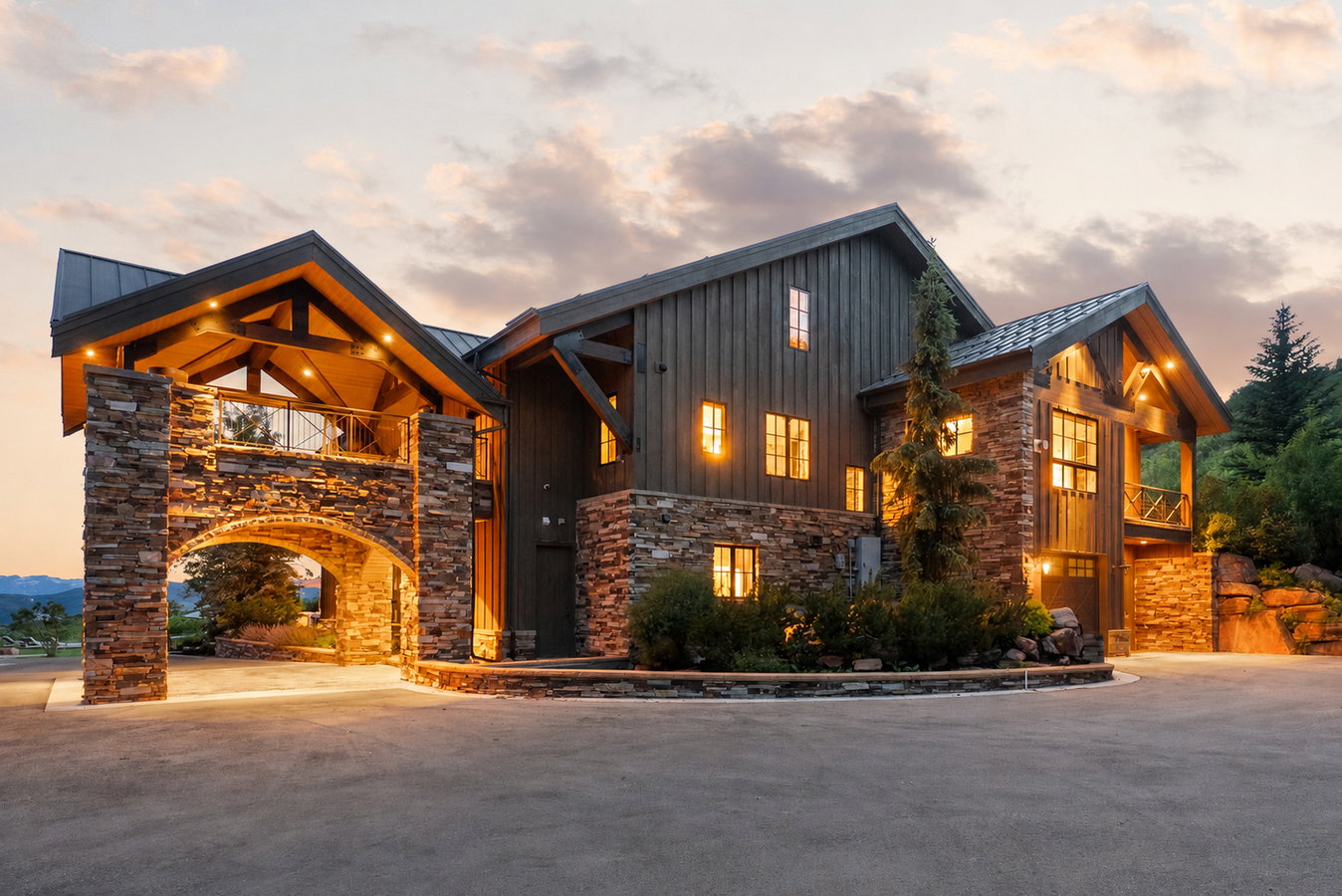 Stone and wood-sided architectural residence featuring a porte-cochere with an upper balcony, exposed timber beams, and a metal roof