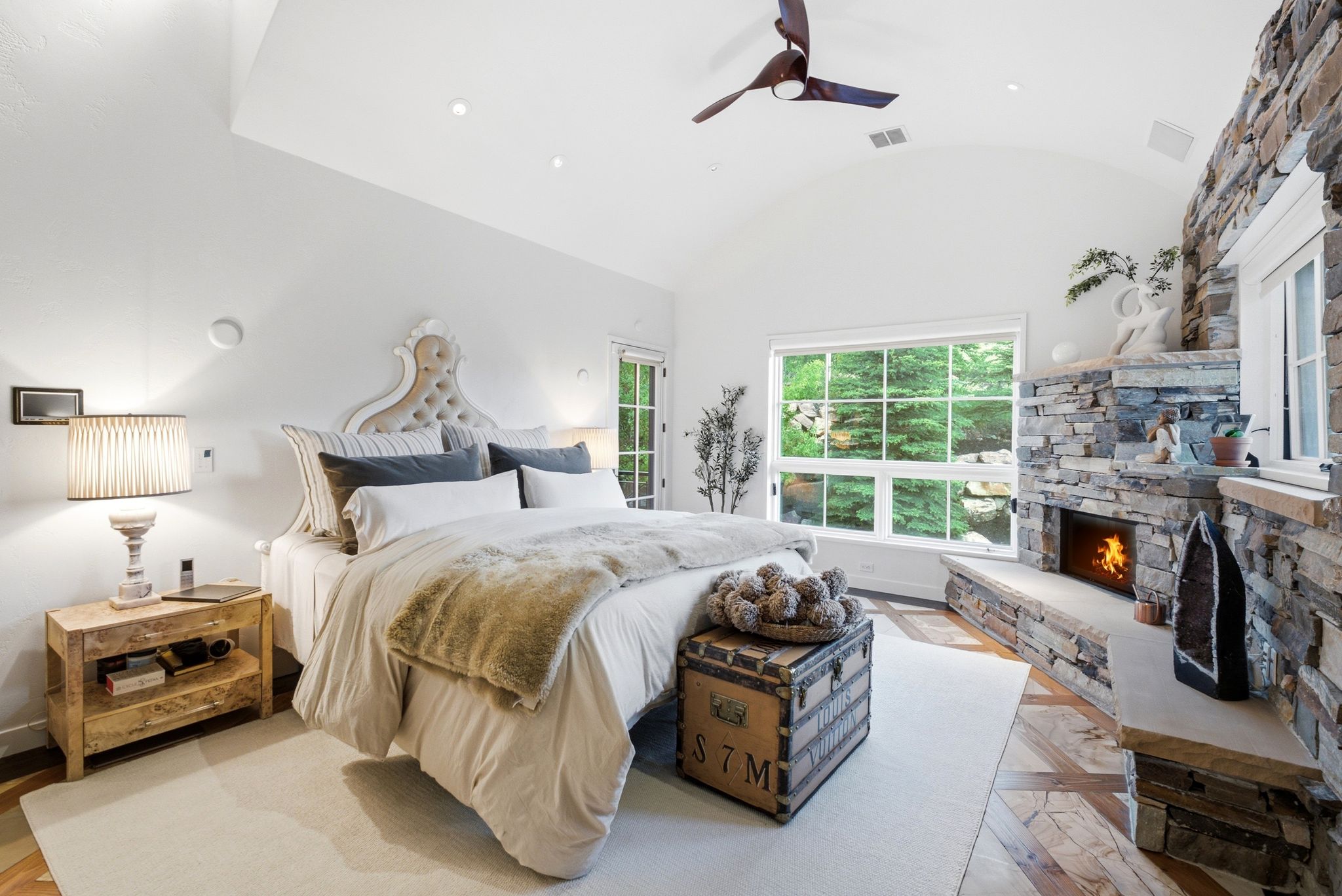 Vaulted ceiling with recessed lighting and a ceiling fan, stone-clad fireplace with a hearth, large window, and wood-finish flooring