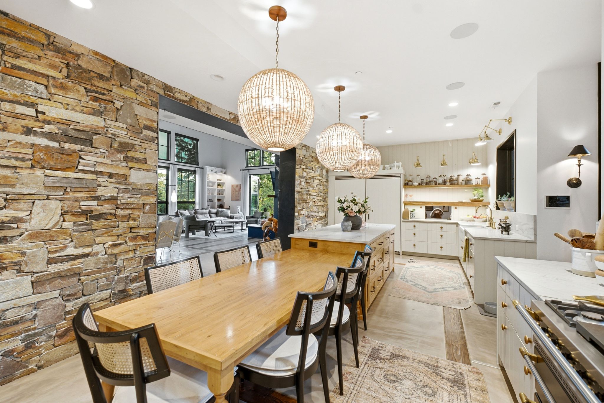 Open-concept dining and kitchen area featuring a stone accent wall, three spherical beaded pendant lights, a gas range with a substantial hood, and extensive cabinetry with gold-toned hardware