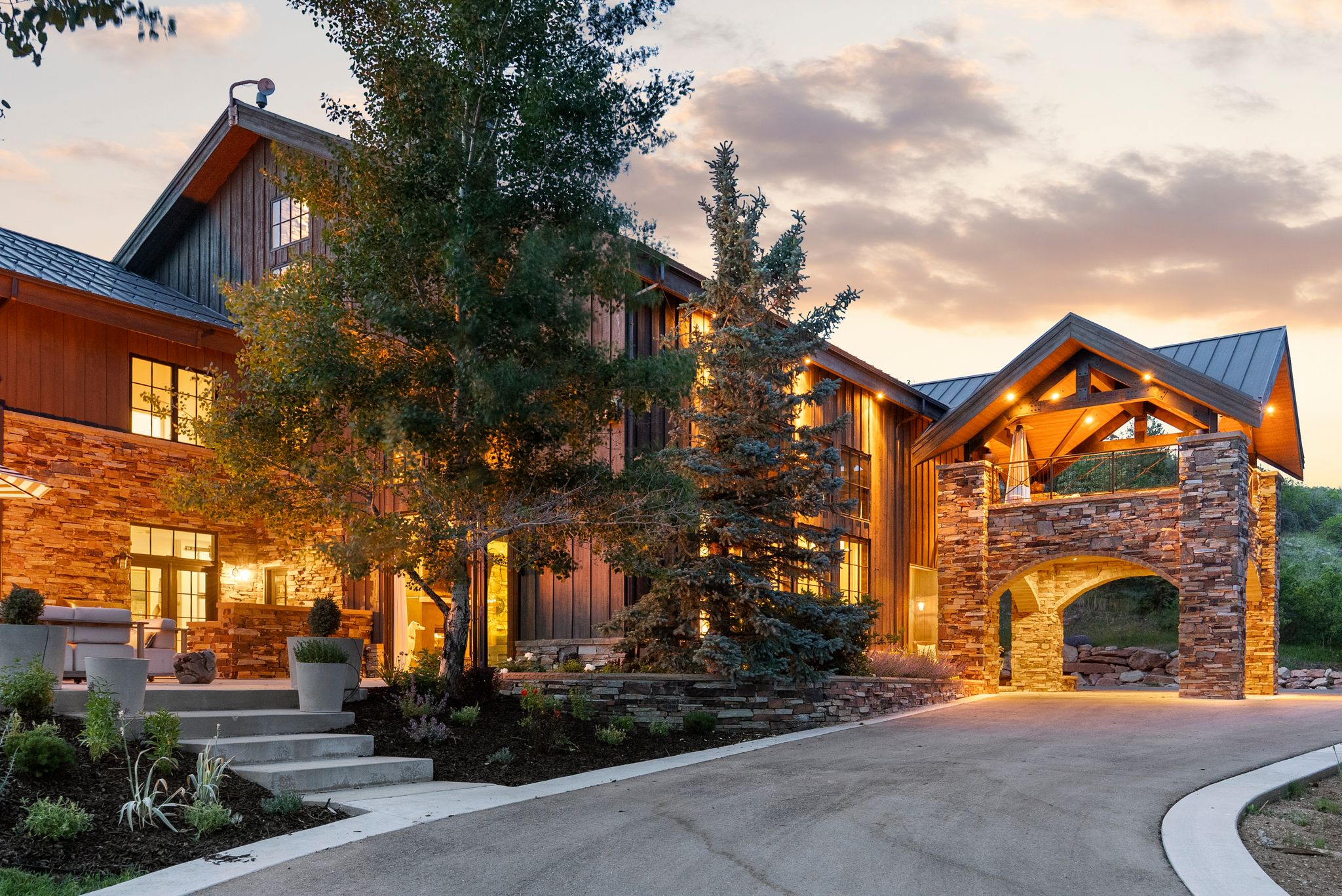 Expansive residence featuring a stone and vertical wood-plank facade, a porte-cochère with stone archway, and a covered entry with exposed beam ceiling