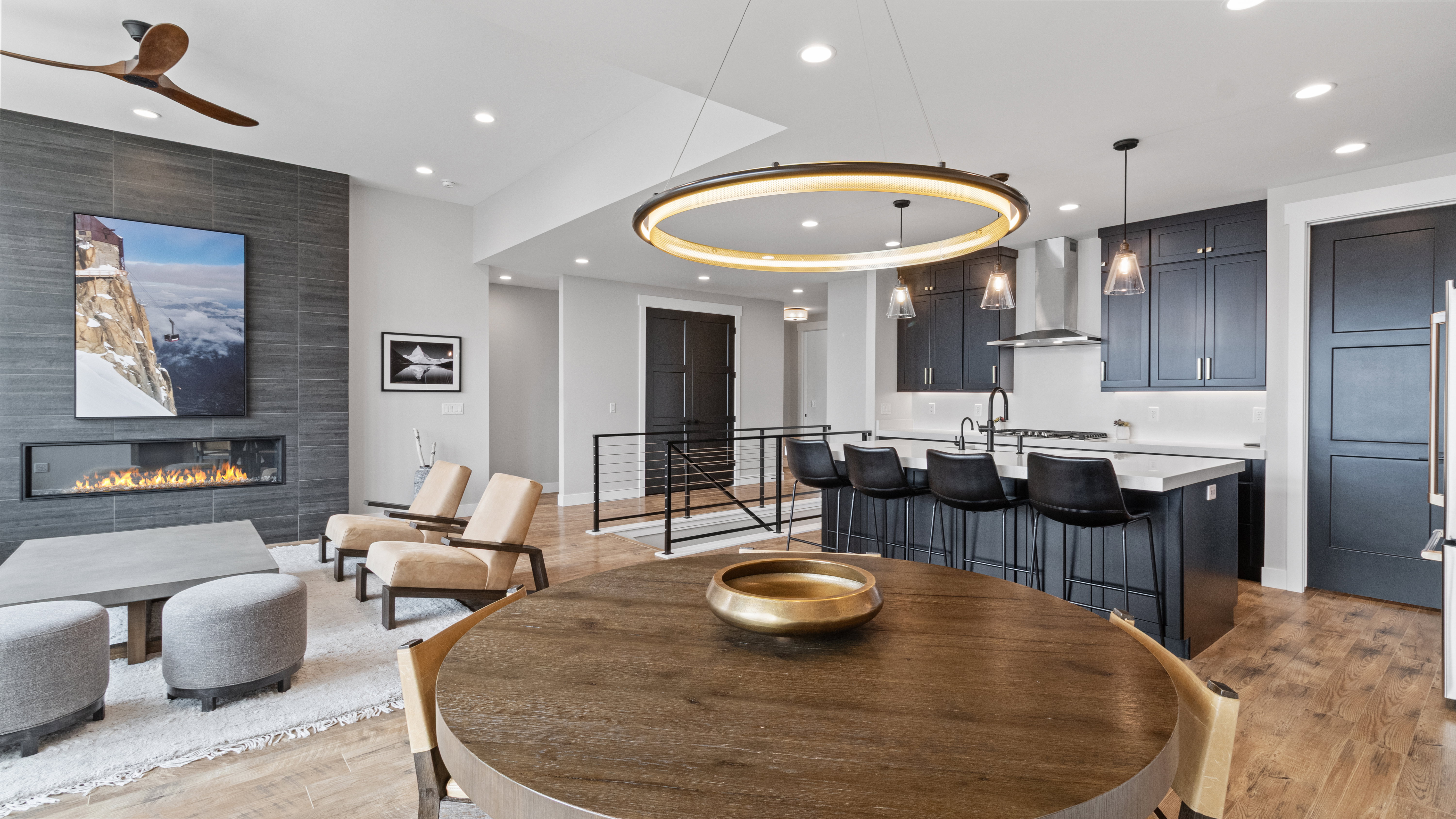 Open-concept living space featuring a linear fireplace with a dark tile surround, a built-in kitchen island with seating, dark cabinetry, pendant lighting, and wood-finish flooring