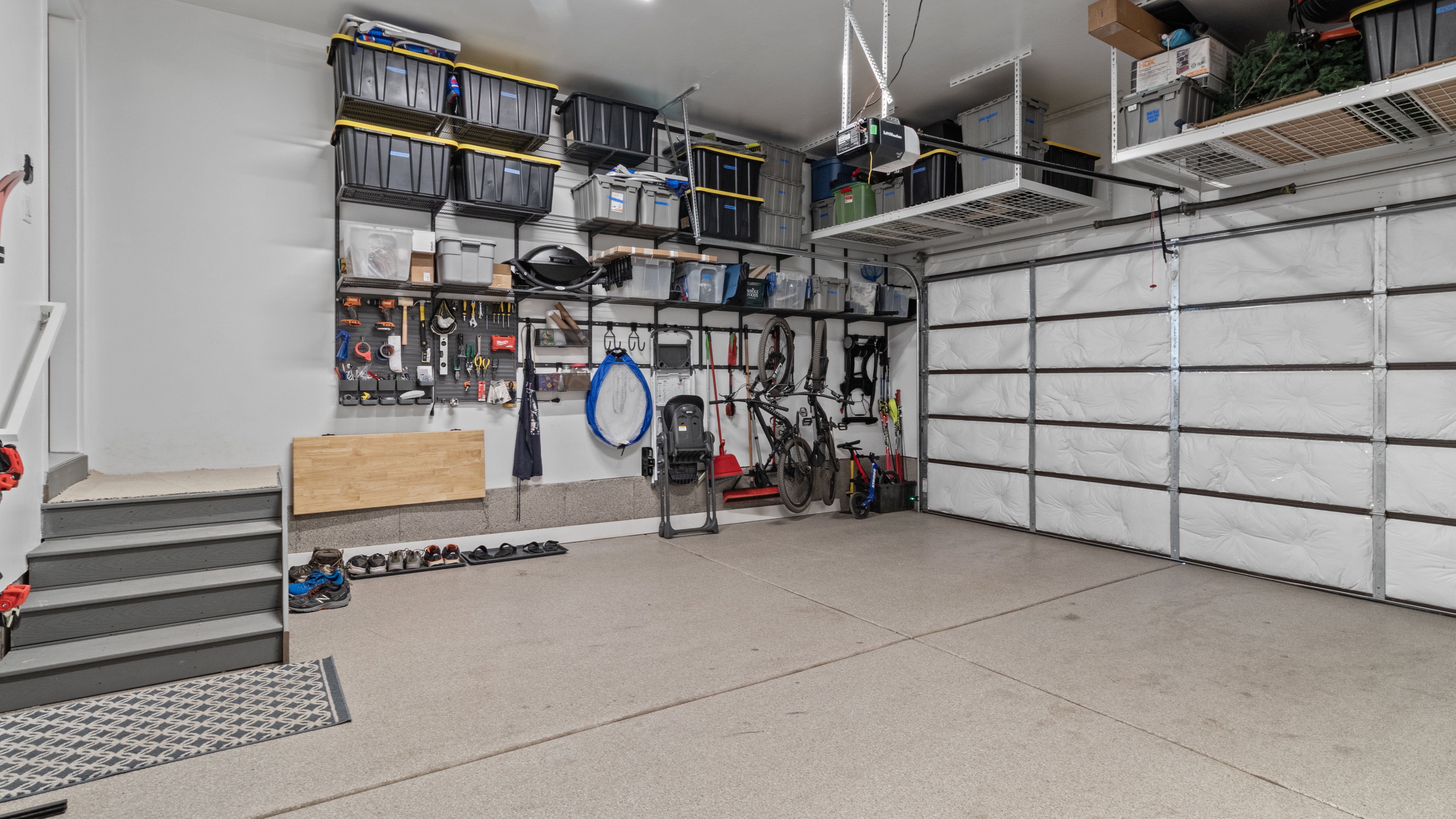 Garage space with outlet for EV charging,  extensive wall-mounted storage systems, overhead shelving, and a durable epoxy-coated concrete floor.