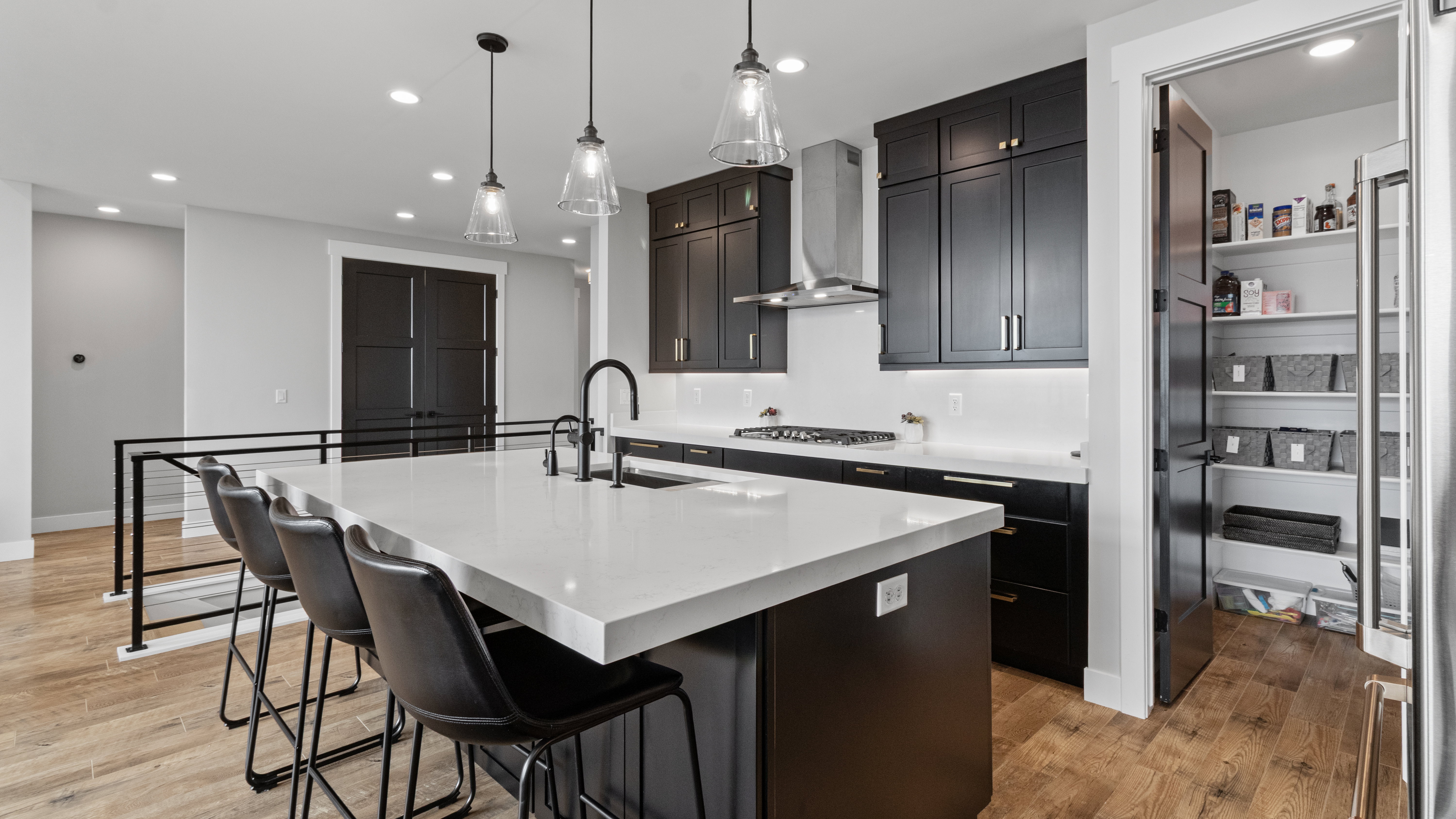 Modern kitchen featuring a large island with seating, a built-in sink with a matte black faucet, pendant lighting, dark cabinetry, and wood-finish flooring