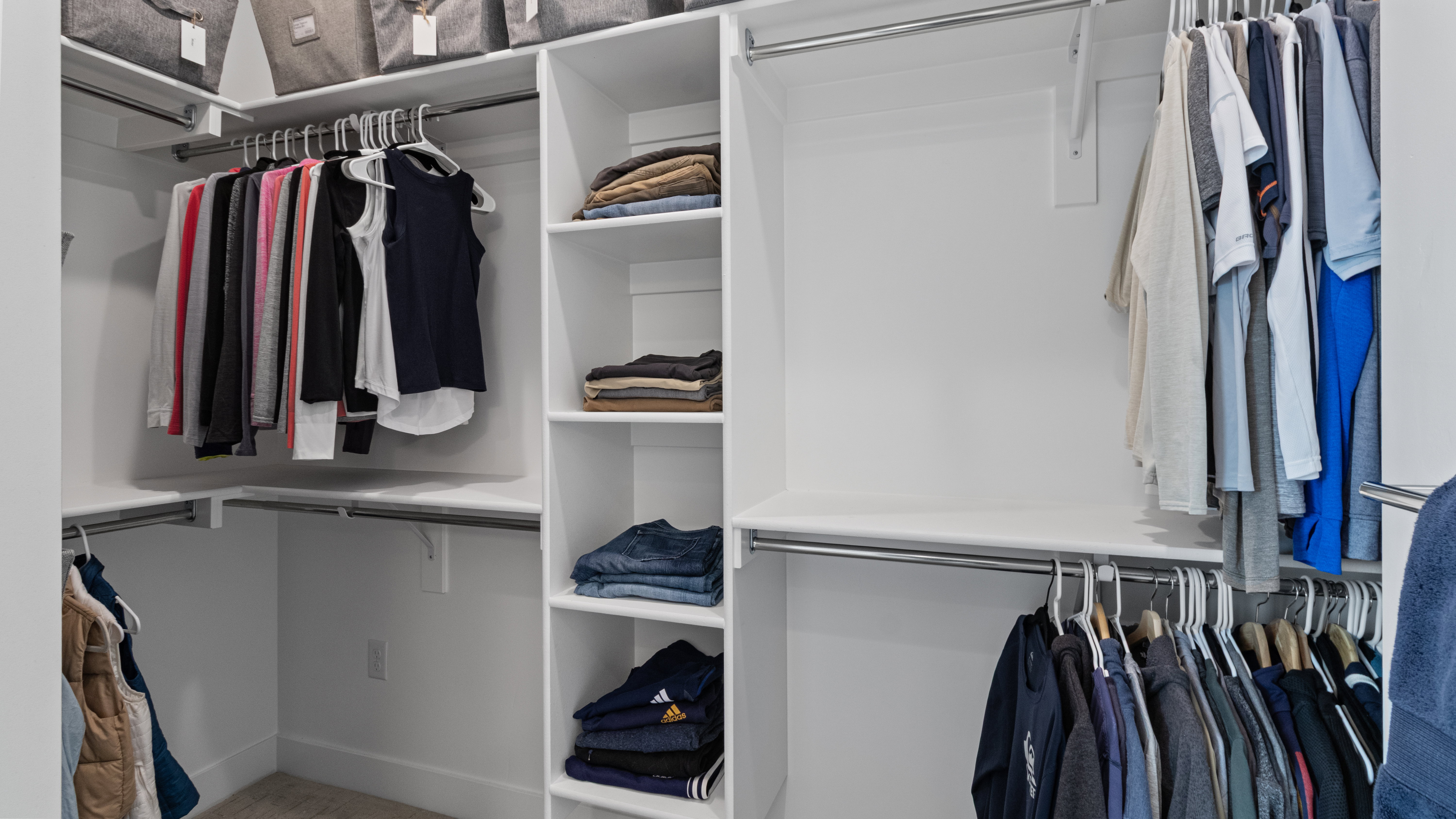 Custom Primary Suite closet system featuring white shelving, multiple hanging rods, corner storage, integrated shelving units, and overhead storage