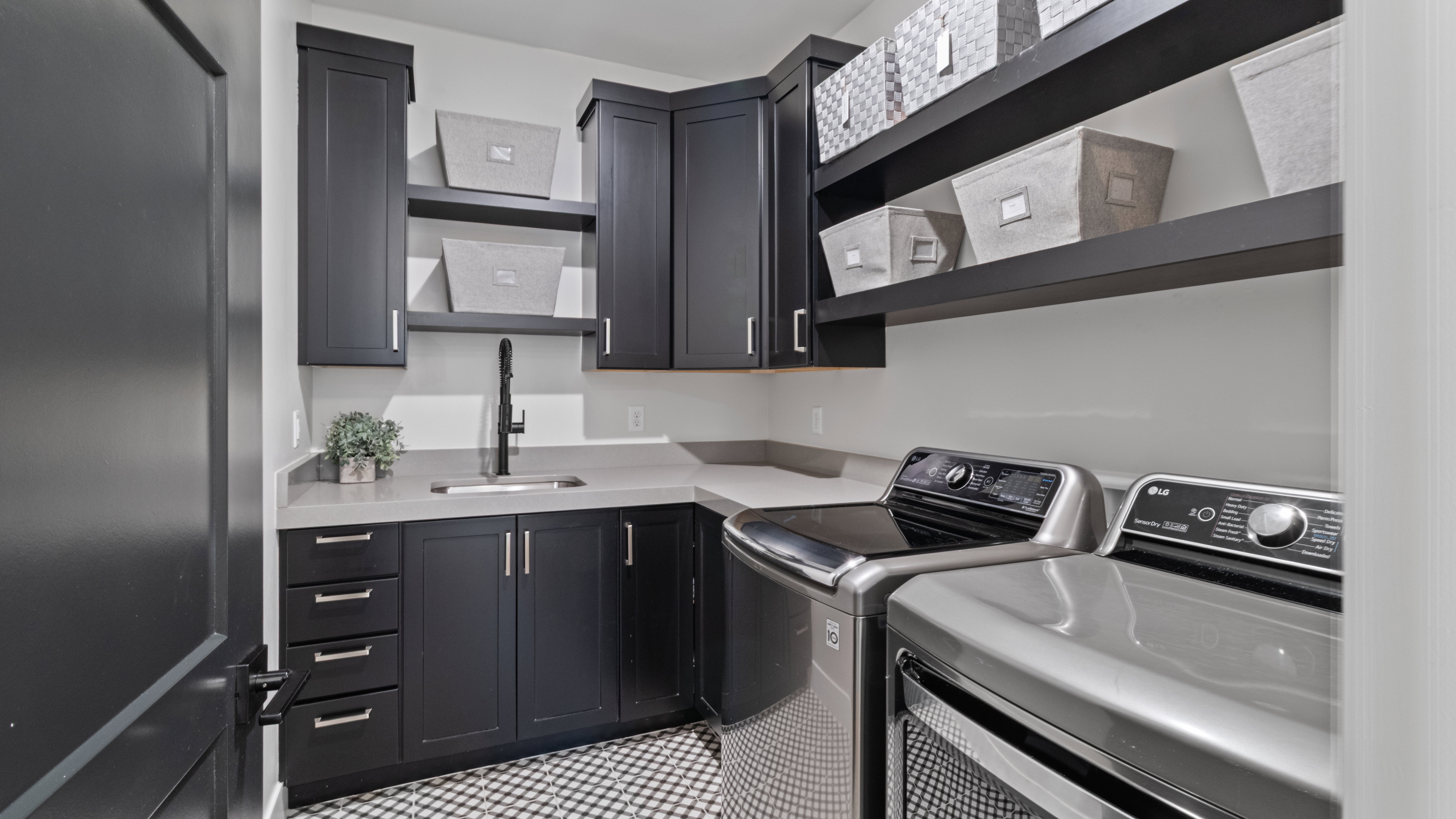 Main level utility room featuring dark cabinetry, light countertops, a utility sink with a matte black faucet, and patterned floor tiling.  Plumbed for both gas and electric.