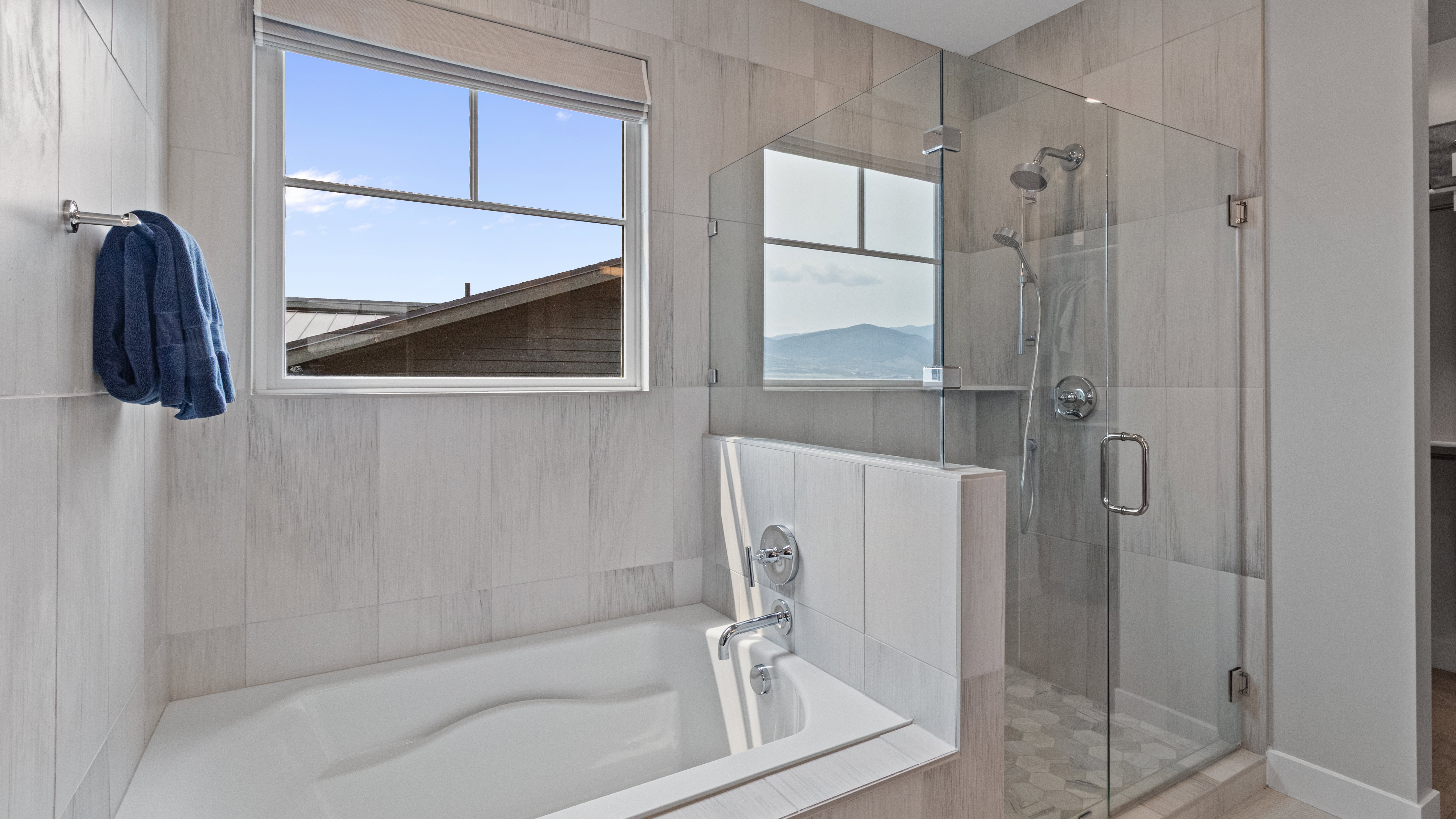 Primary suite's modern bathroom featuring a built-in tub, a glass-enclosed shower with a rainfall showerhead, and light-toned tile finishes