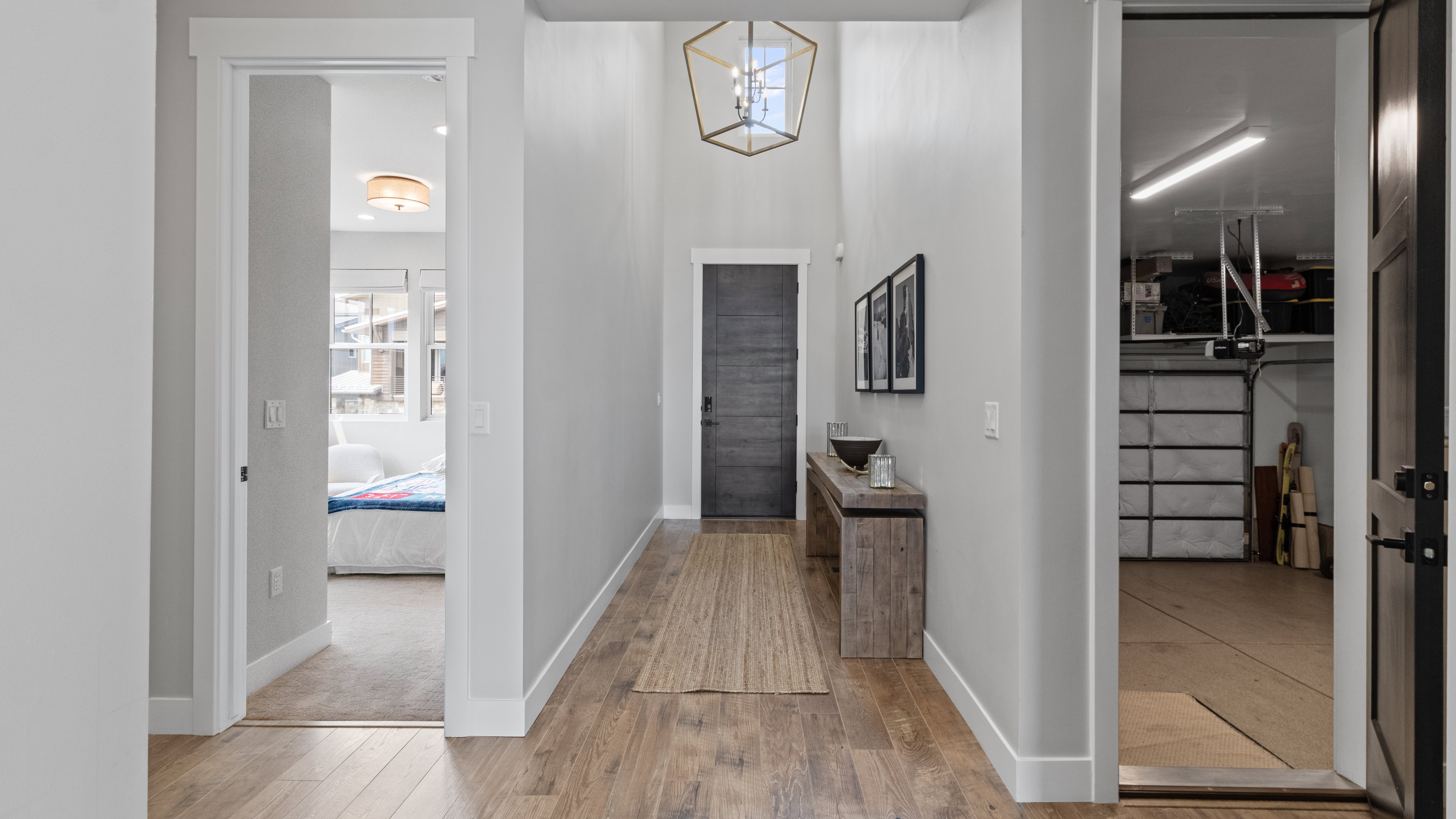 Entry hallway looking towards the front door.  Wood-finish flooring, a contemporary geometric chandelier, and tall ceilings