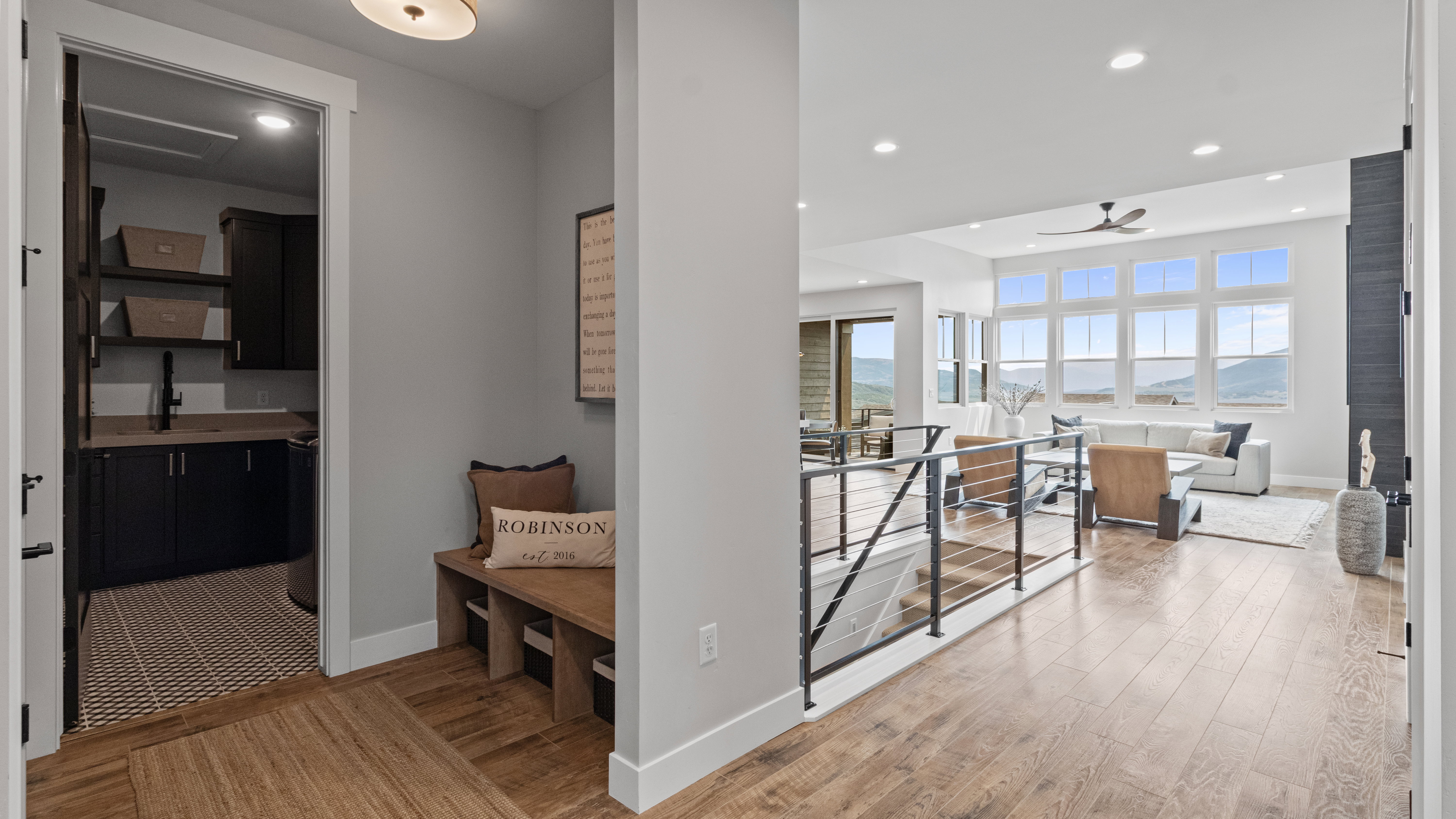 Entry hall with wood-finish flooring throughout, with a built-in wooden bench and a utility room featuring dark cabinetry and a patterned floor