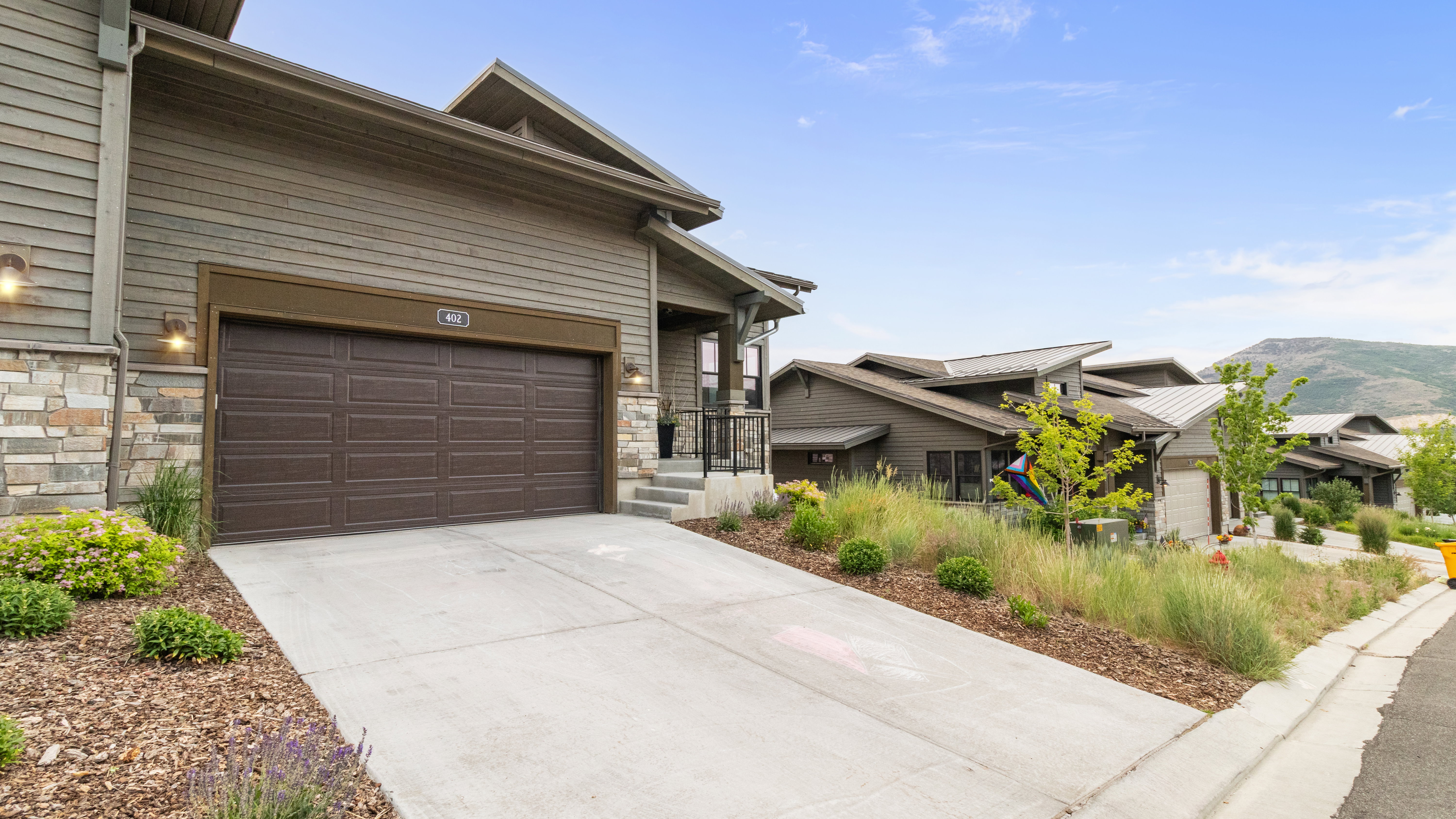 Exterior facade featuring horizontal siding, natural stone accents, a two-car garage, and integrated outdoor lighting fixtures