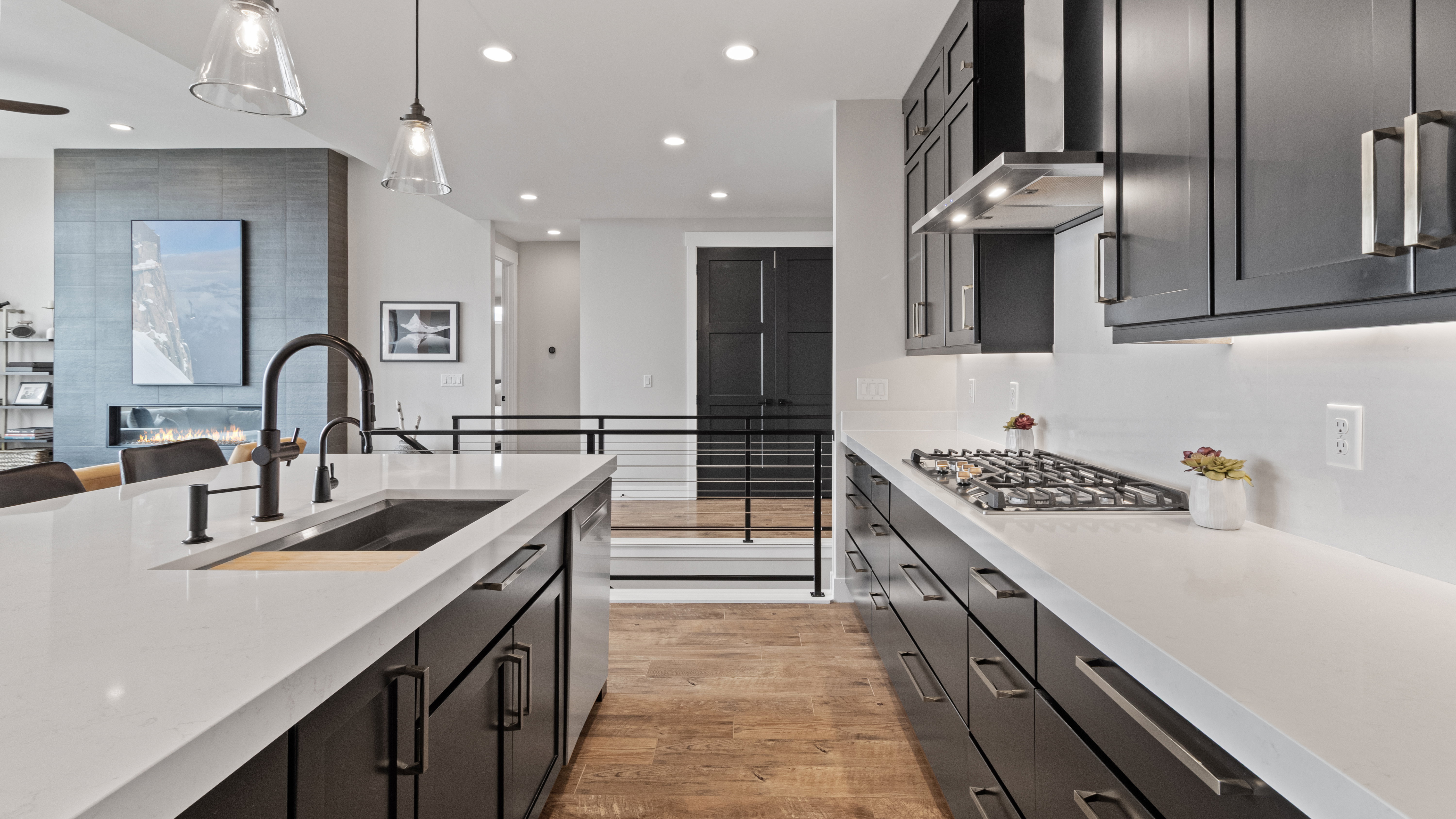 Contemporary kitchen featuring an oversized island with an integrated sink, dark wood-finish cabinetry, a gas cooktop, and light-toned countertops with a matching backsplash