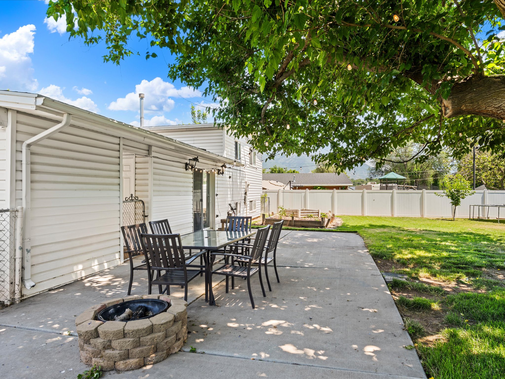 Spacious concrete patio featuring a built-in fire pit, string lighting, and a mature shade tree