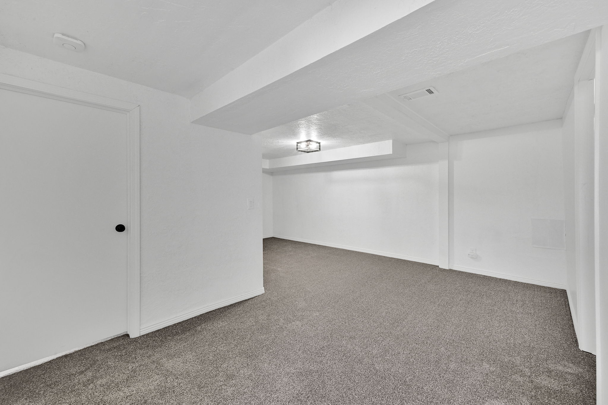Spacious interior featuring fresh white paint, gray carpeting, a contemporary flush mount light fixture, and white trim